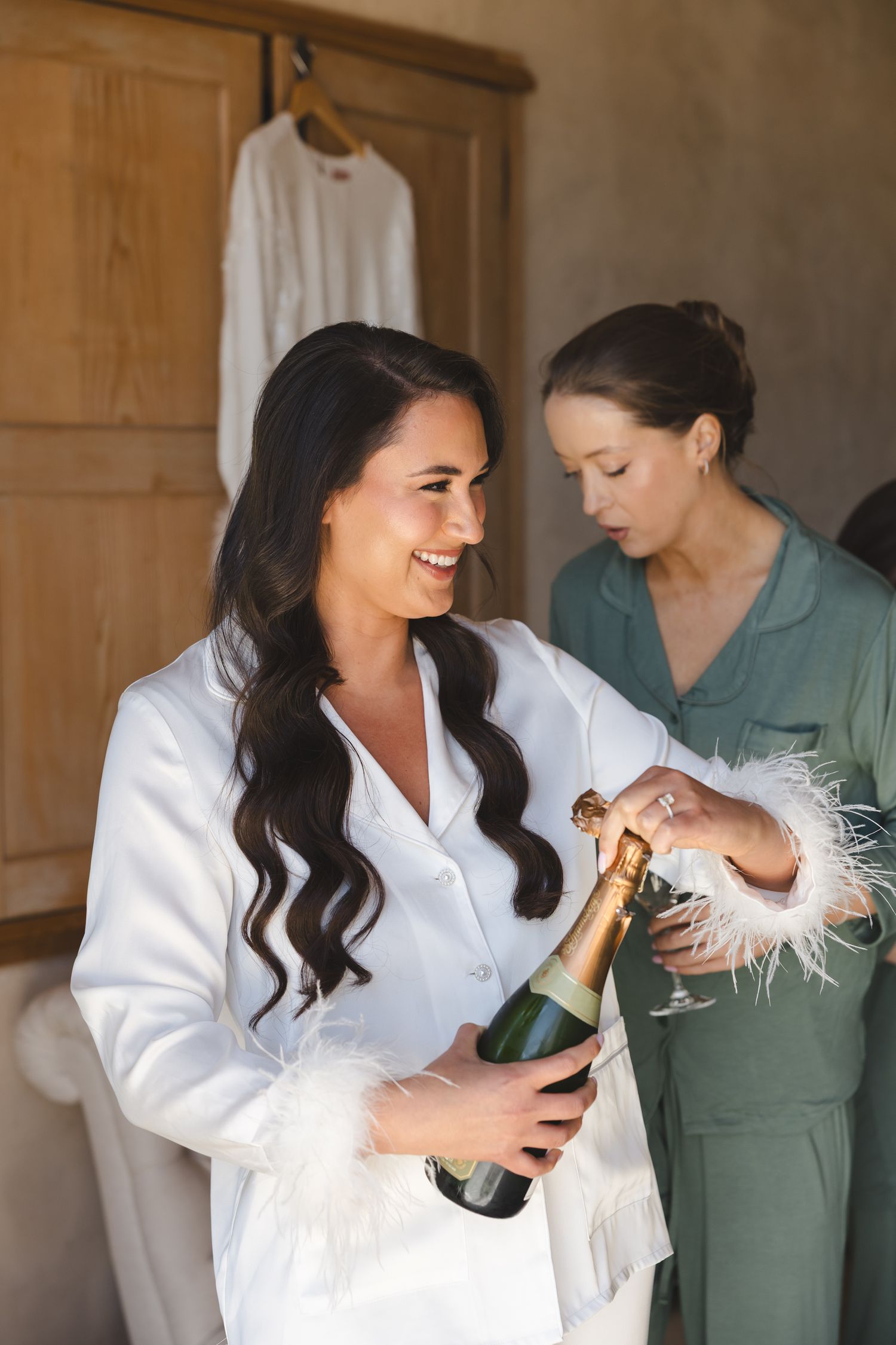 Wedding preparation scene with champagne and white feather trim robes in a rustic room.