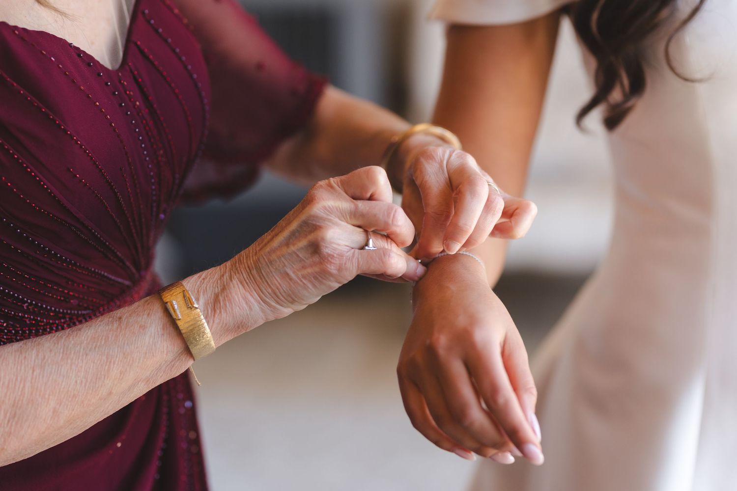 Close-up shot of hands adjusting jewelry against burgundy and white fabric.