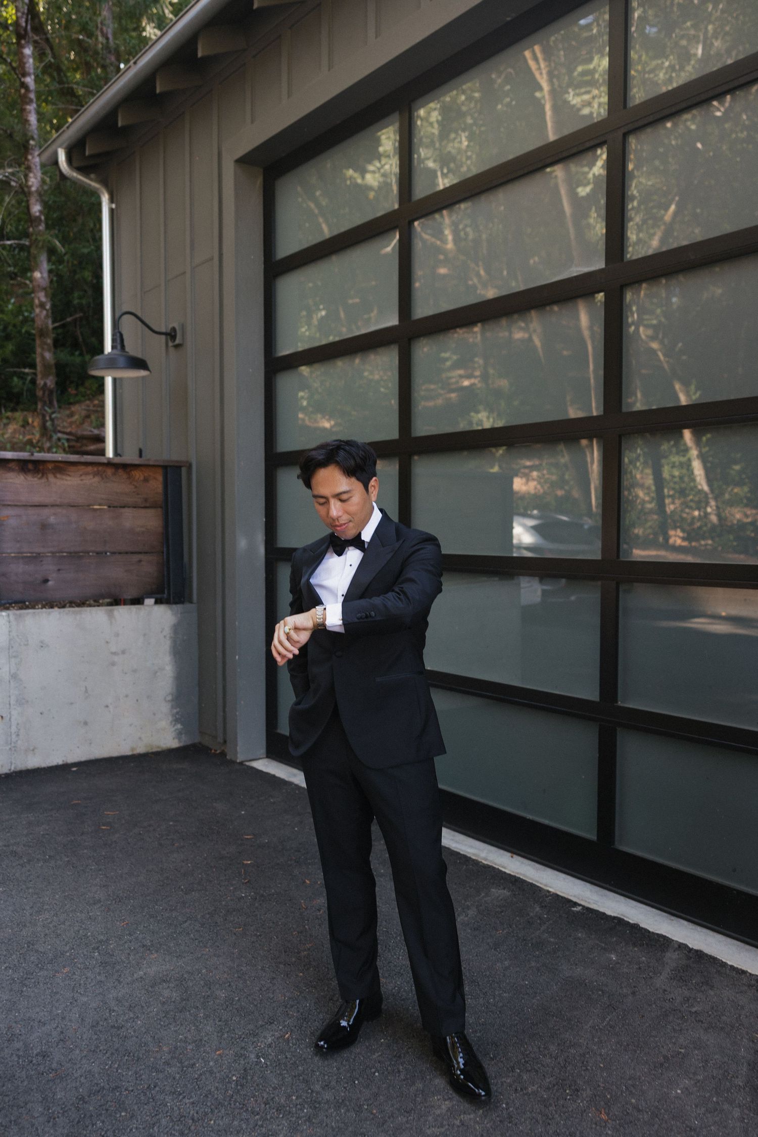 Figure in formal attire adjusting clothing near a modern glass wall building.