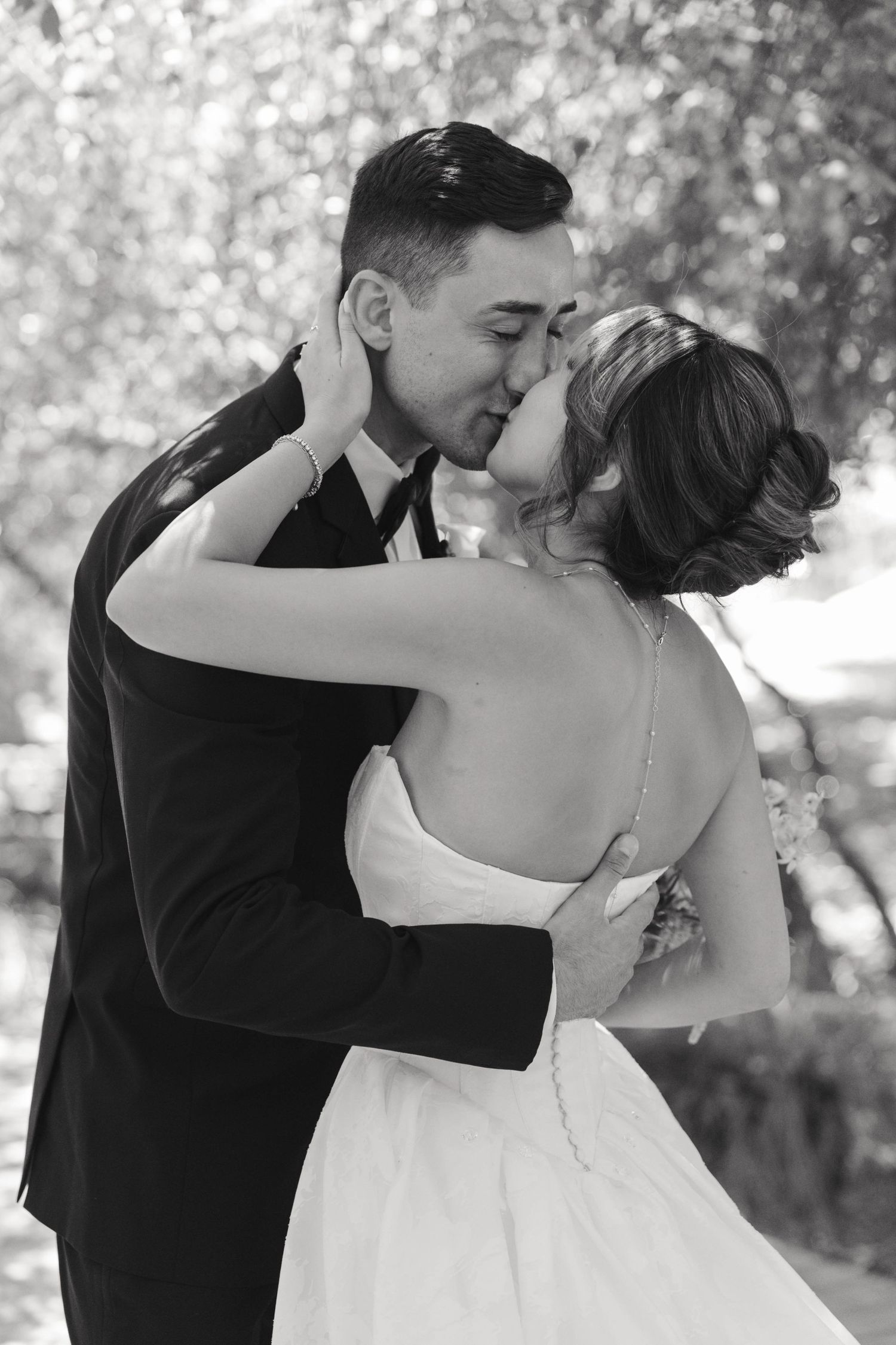 Black and white romantic kiss between newlyweds in garden setting.