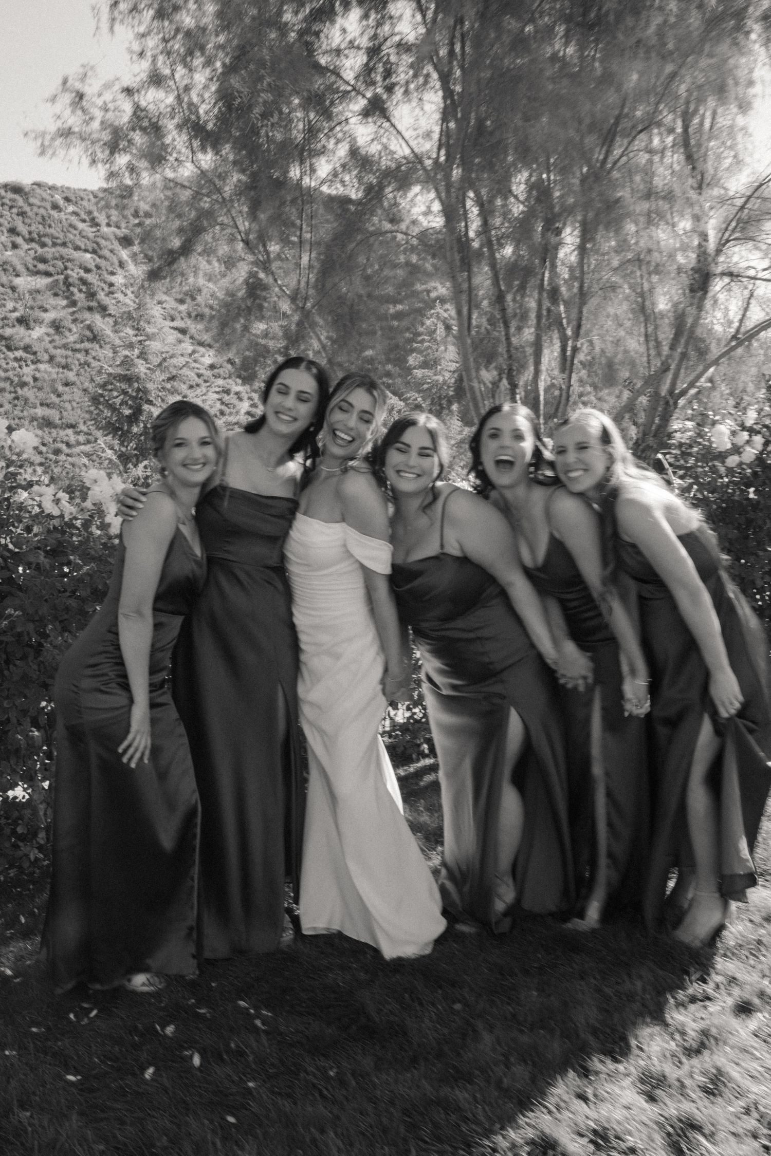 Group photo of wedding party wearing black and white dresses posing outdoors.