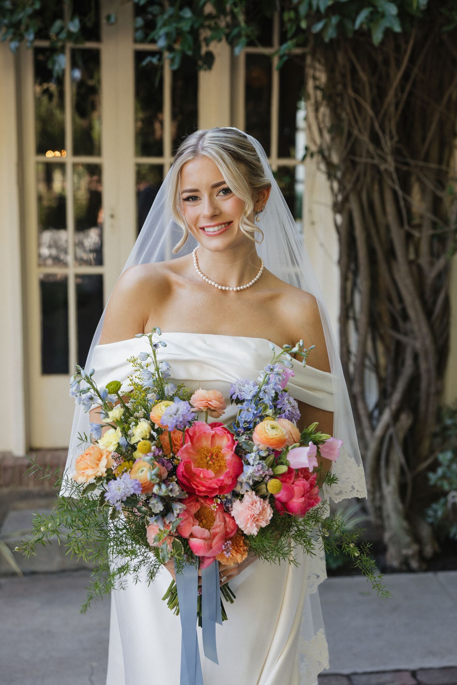 Elegant bridal bouquet features coral, pink and purple flowers with cascading blue ribbons.