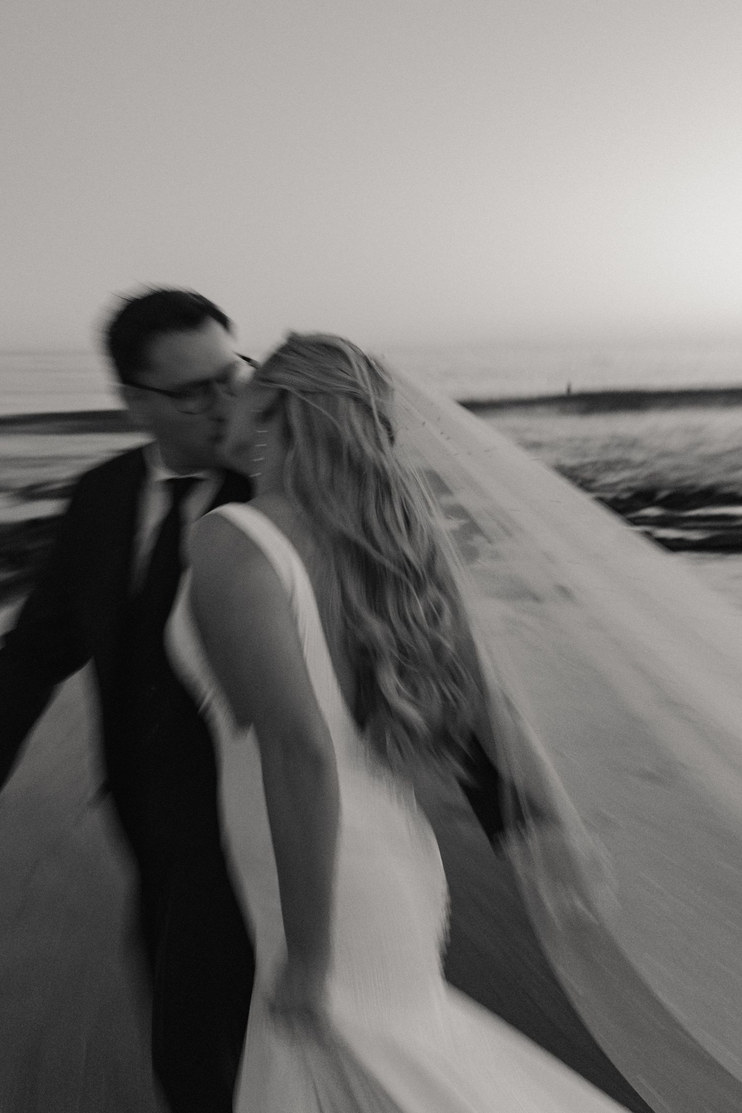 A series of black and white photos showing a figure in a white dress walking along a beach in motion blur.