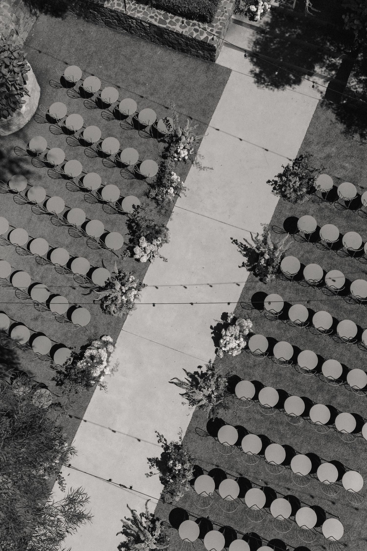 Aerial black and white view of outdoor wedding ceremony chairs arranged in rows with a central aisle and floral arrangements.