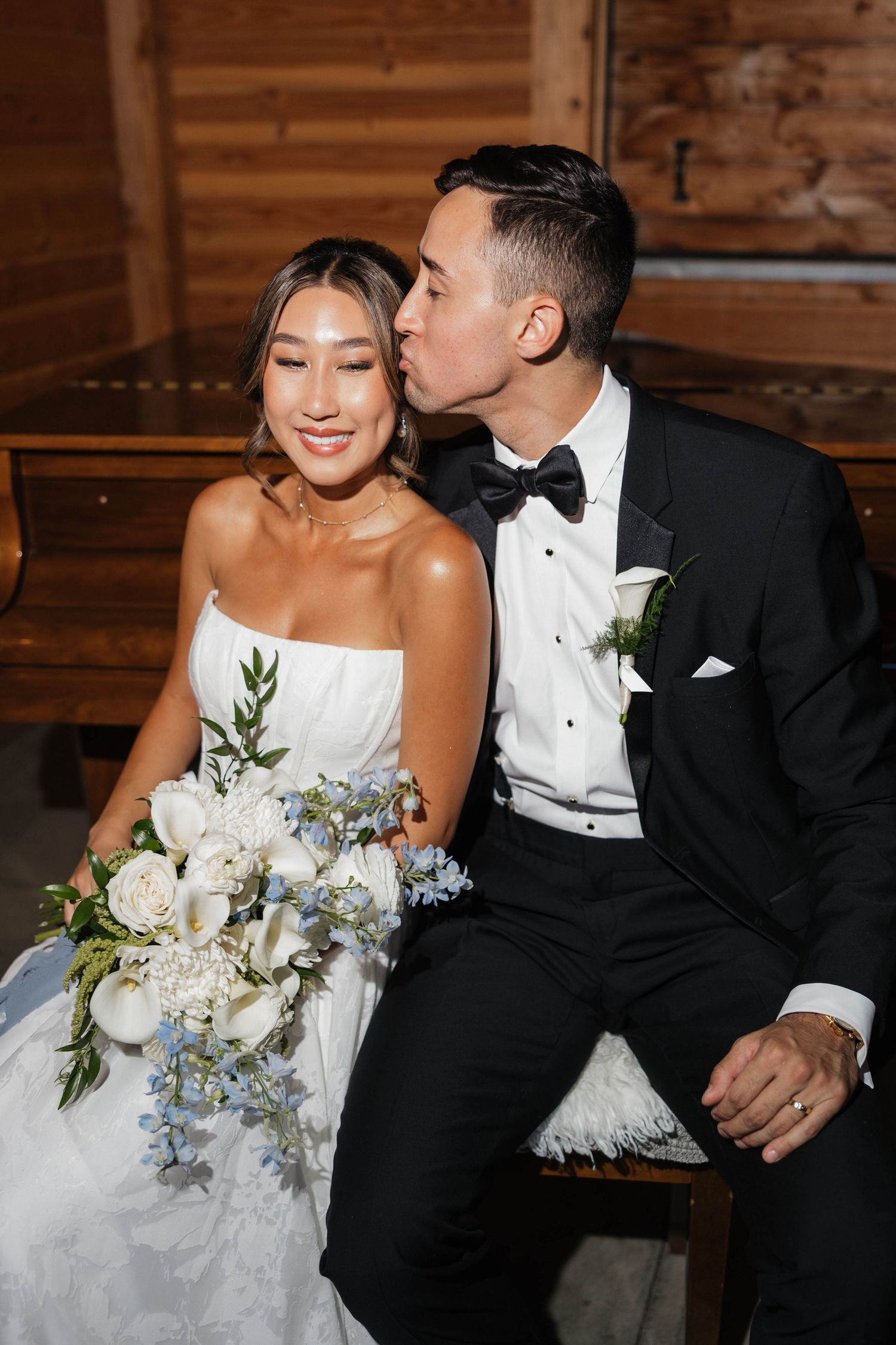 Wedding couple shares intimate moments on wooden bench in rustic barn setting.