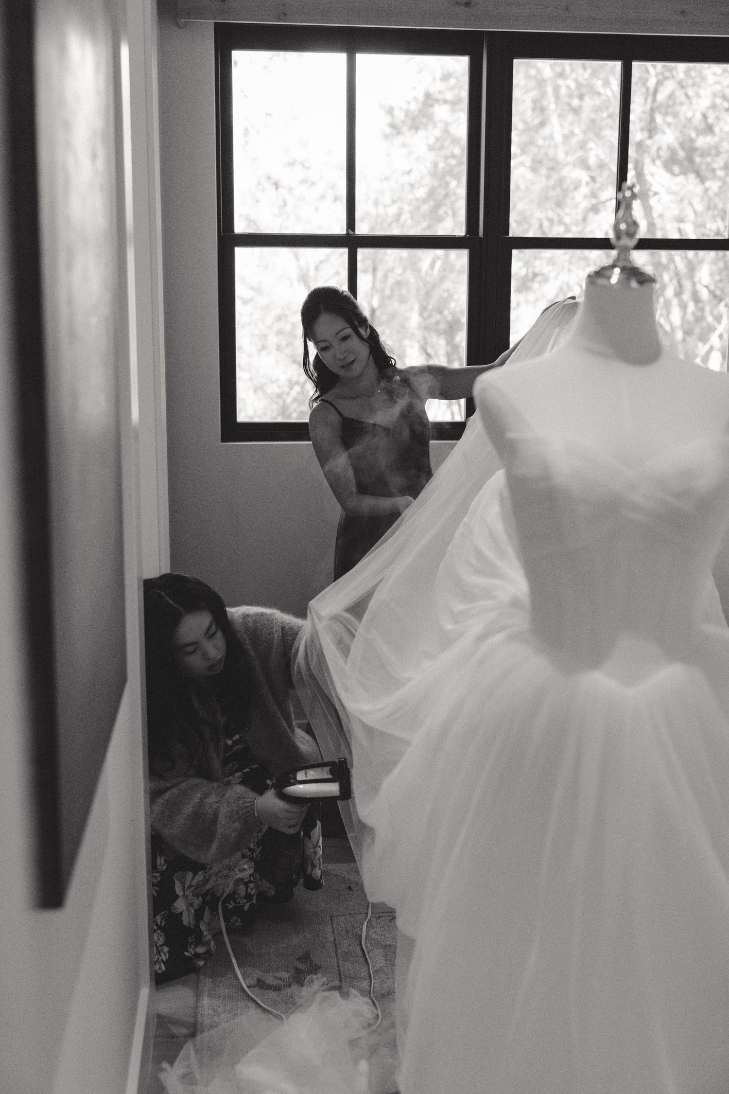 Multiple wedding dresses displayed on hangers in a bridal boutique with natural light streaming through windows.