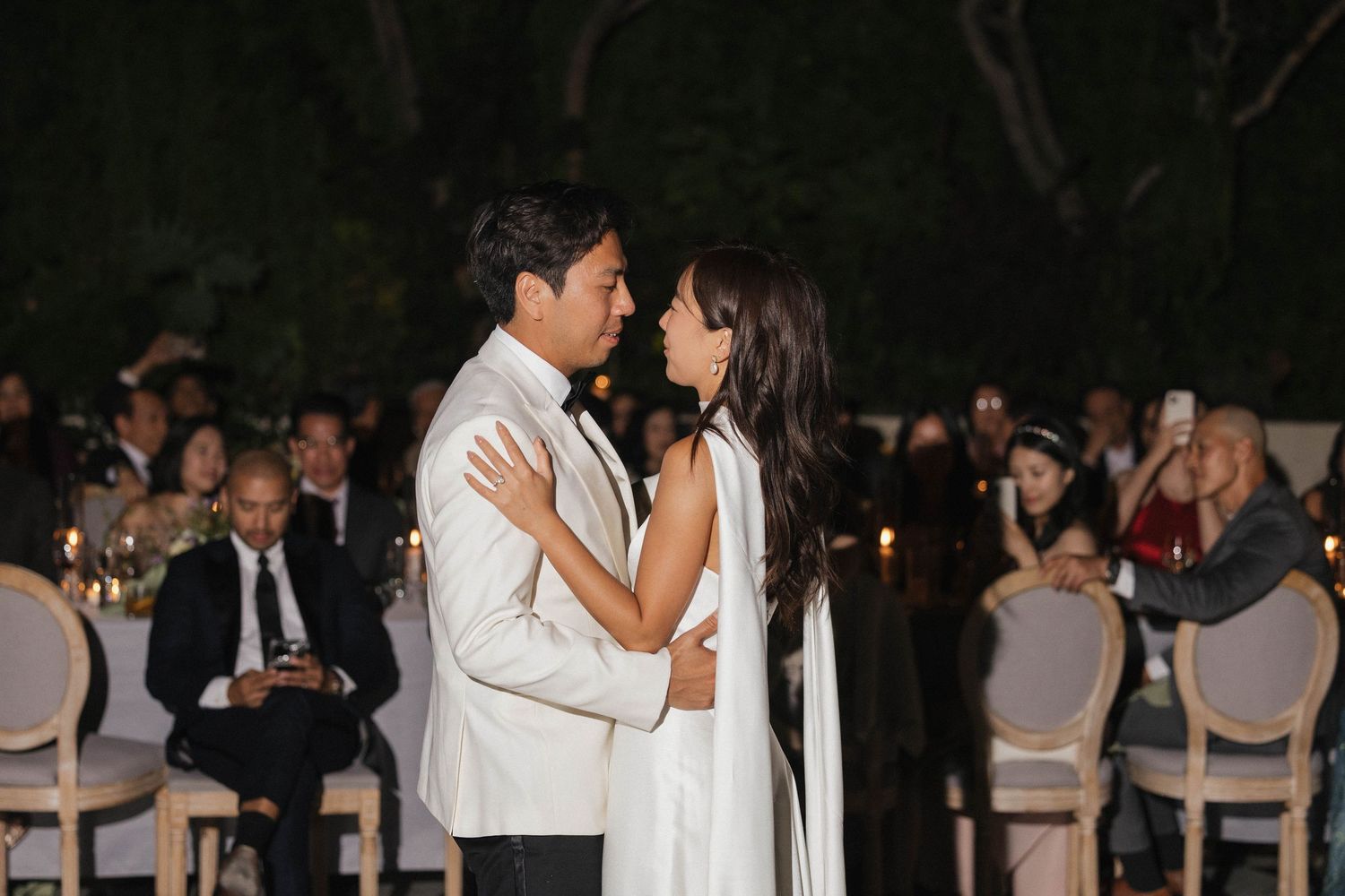 Wedding guests gather for an evening celebration under outdoor lighting.