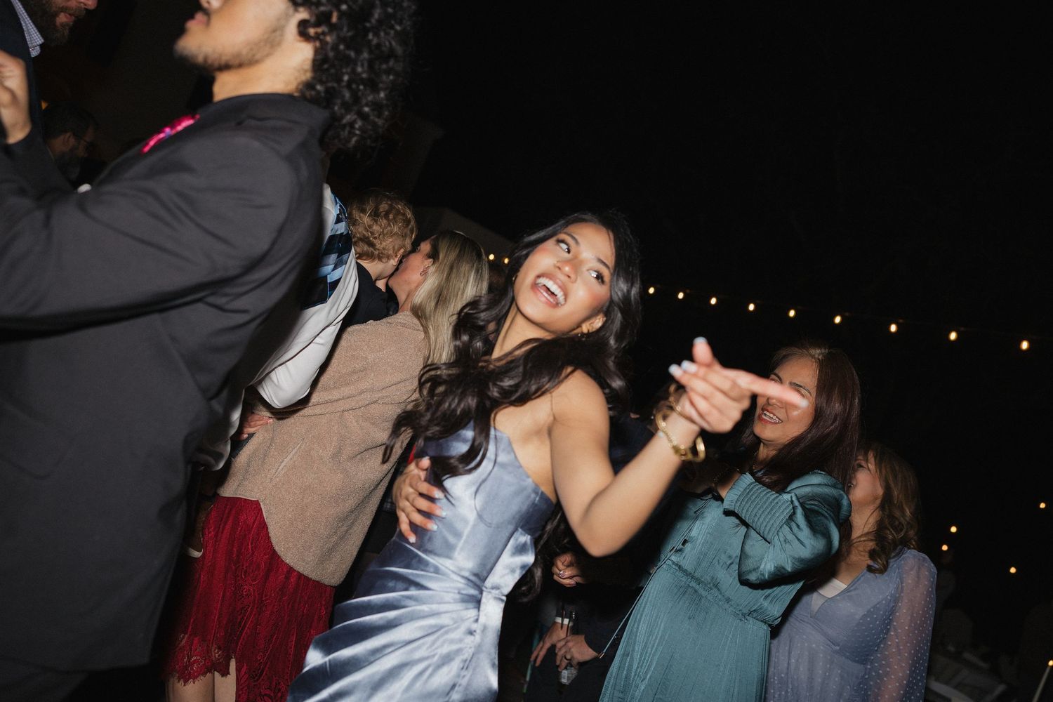 Wedding guests dance and celebrate at a nighttime reception under string lights.