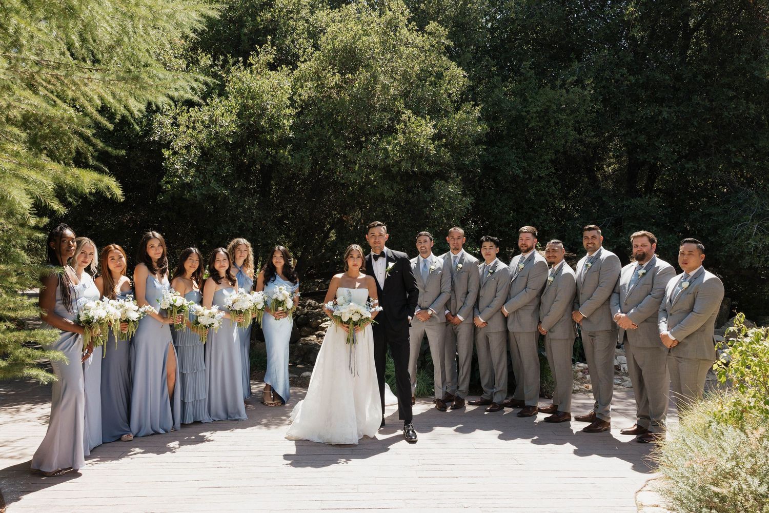 Wedding party lined up outdoors wearing coordinated gray and white attire.