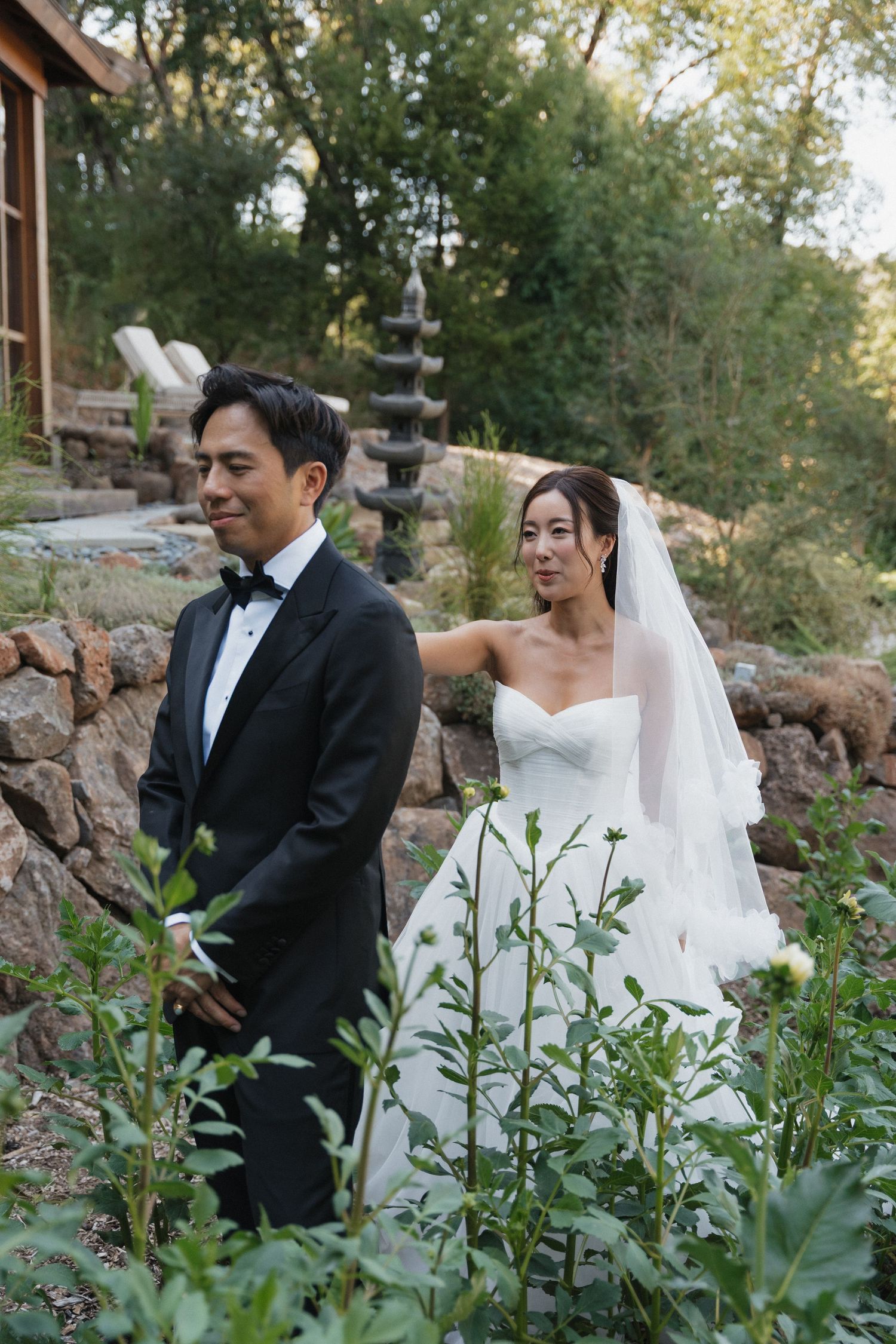 Newlyweds share intimate moments in a garden setting surrounded by greenery.