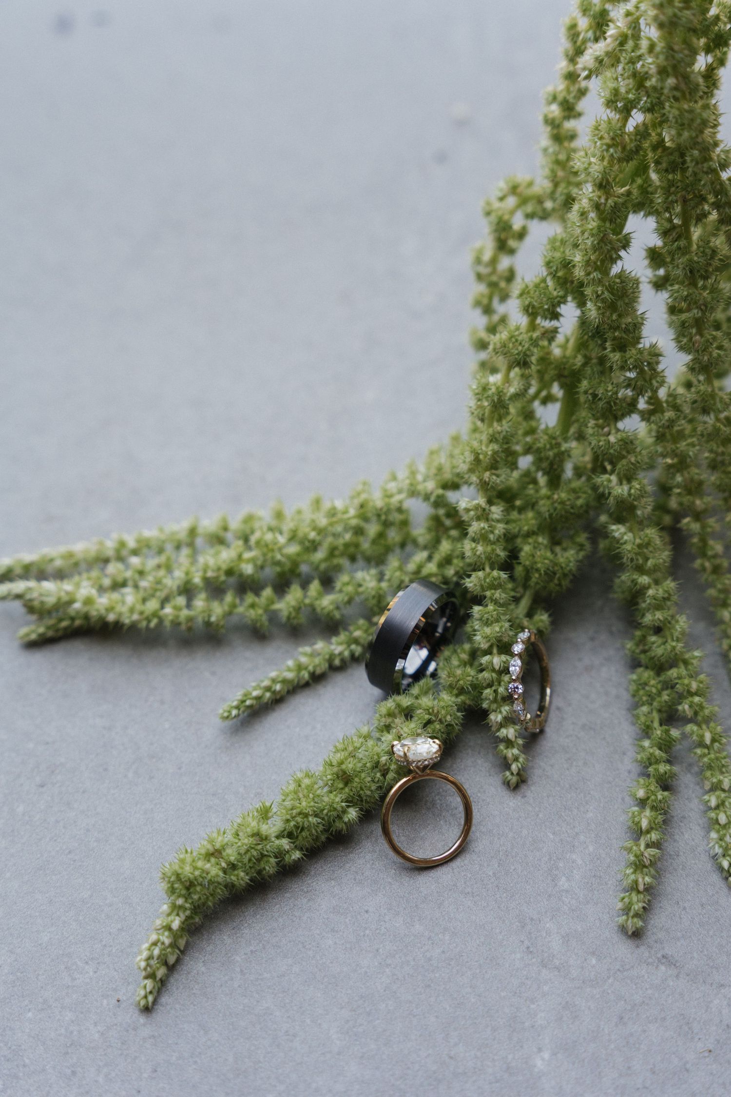Close-up of a delicate ring displayed on green floral stems against a gray background.