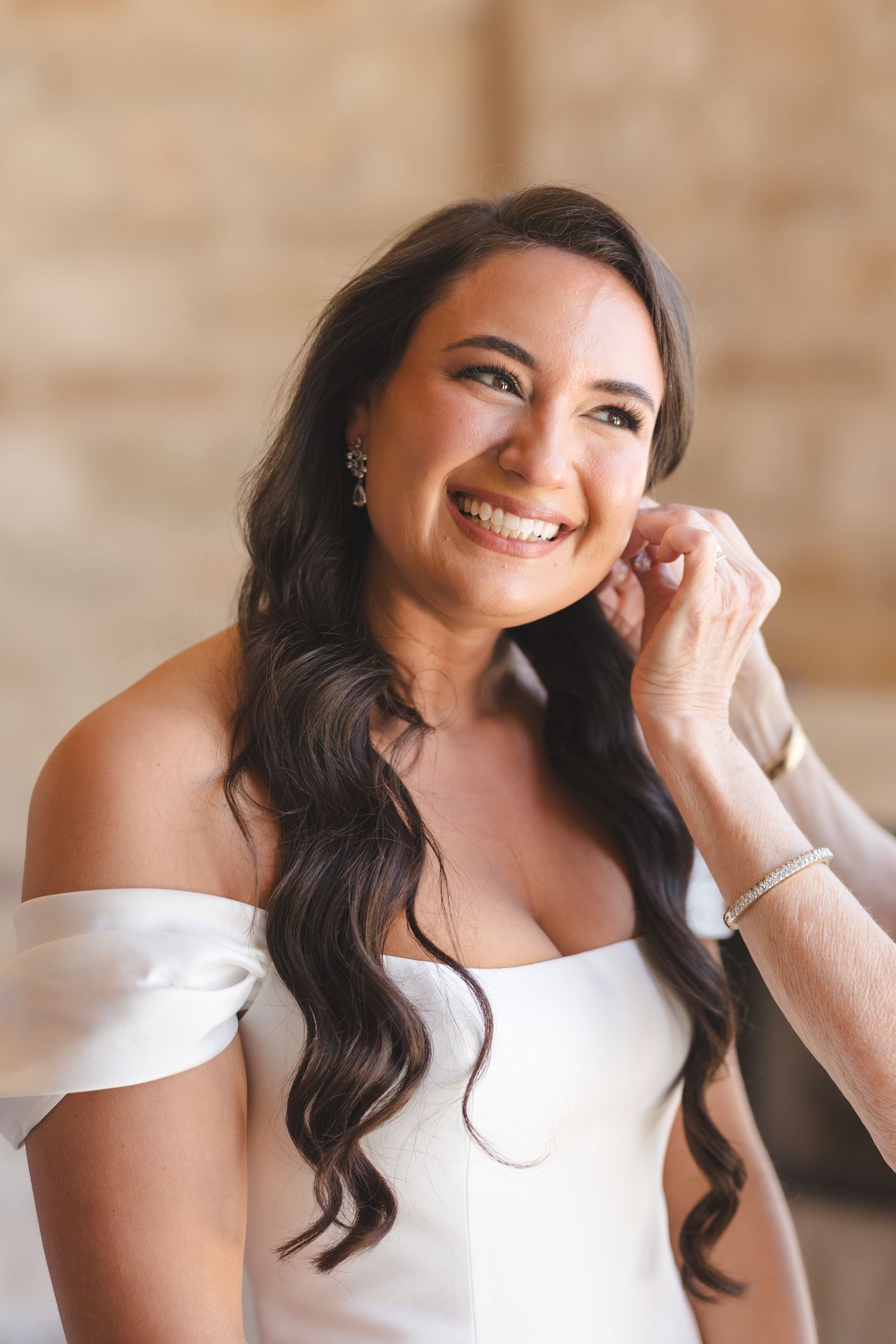 Bride in off-shoulder white wedding gown with long dark wavy hair.