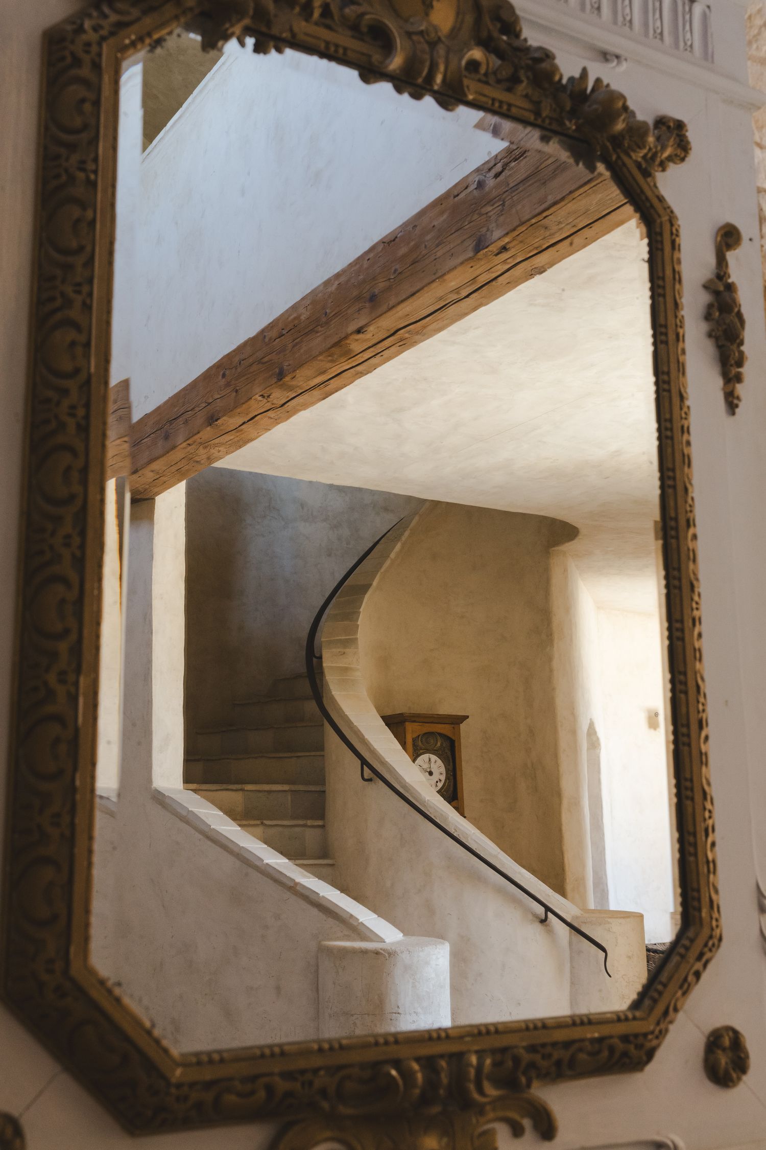 Ornate vintage mirror reflects curved staircase in elegant interior.