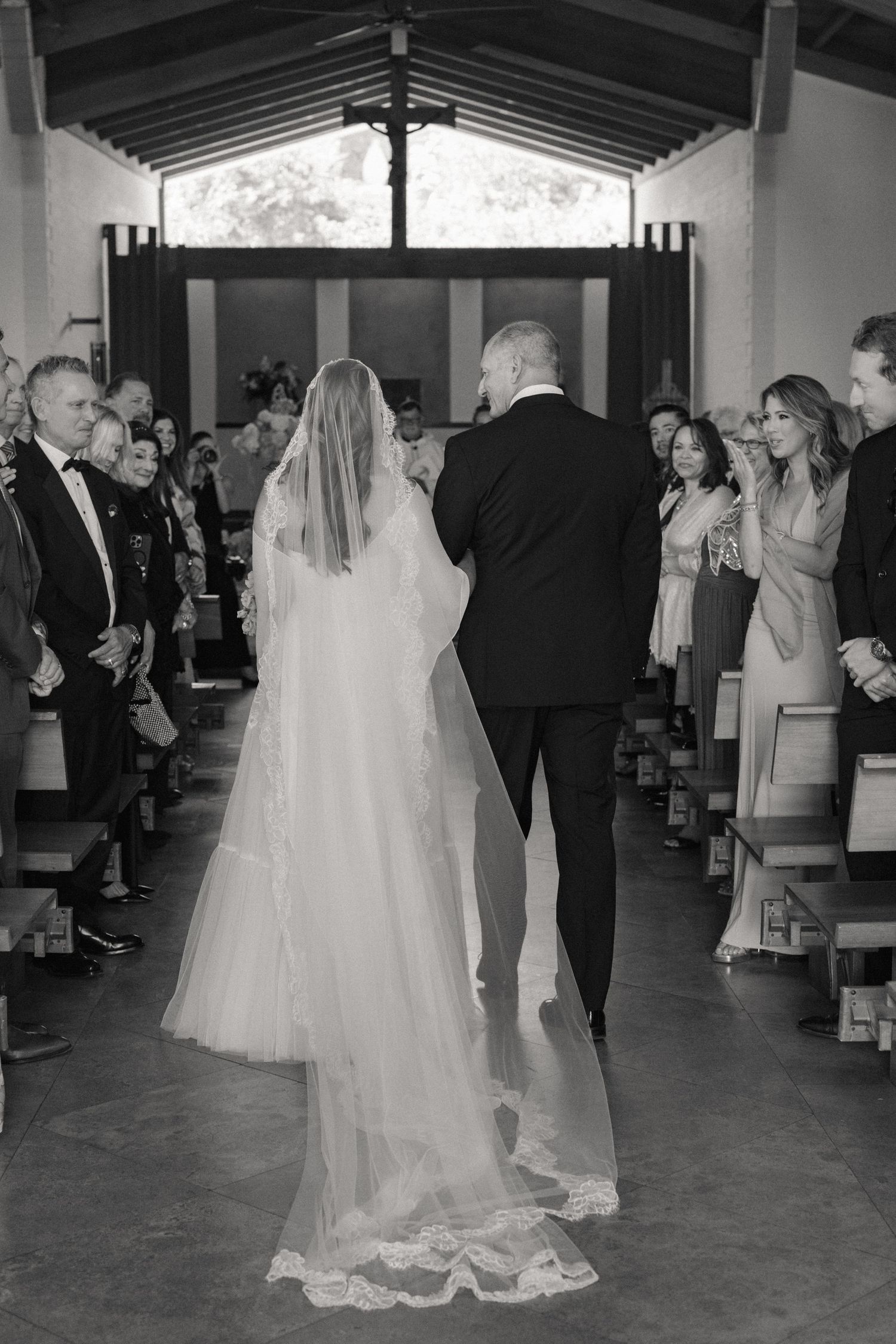 Black and white photo of bride and groom walking down church aisle at wedding ceremony.