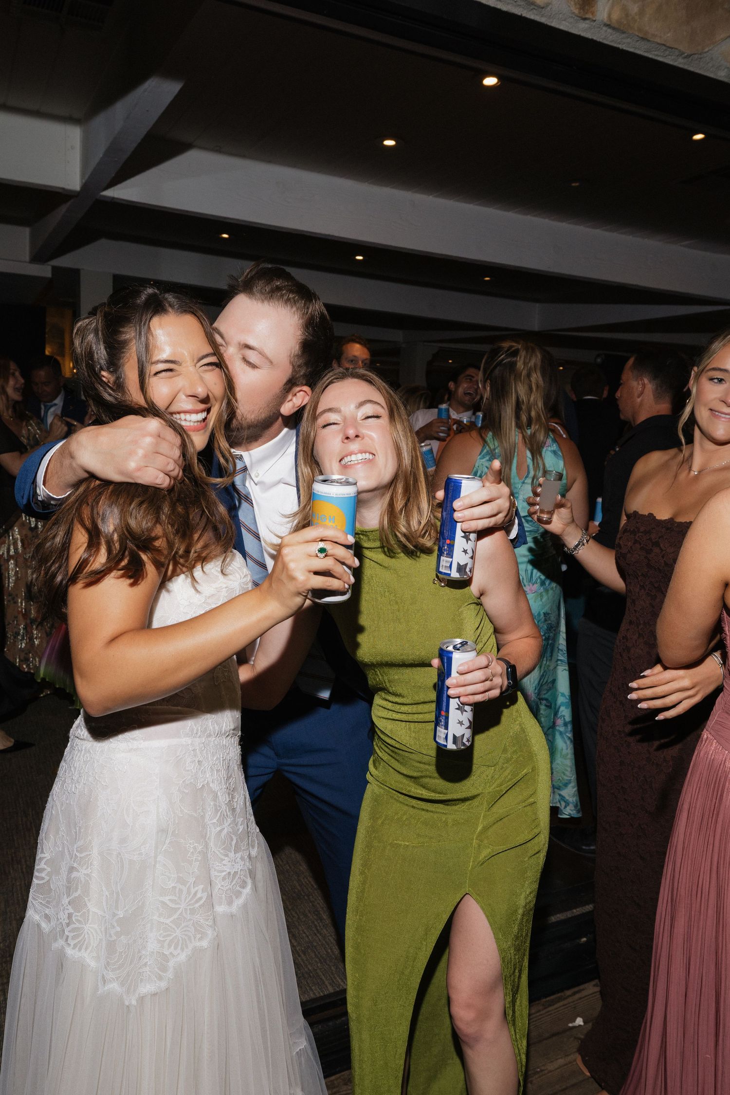 Joyful bride and groom celebrate with guests on wedding dance floor holding drinks.