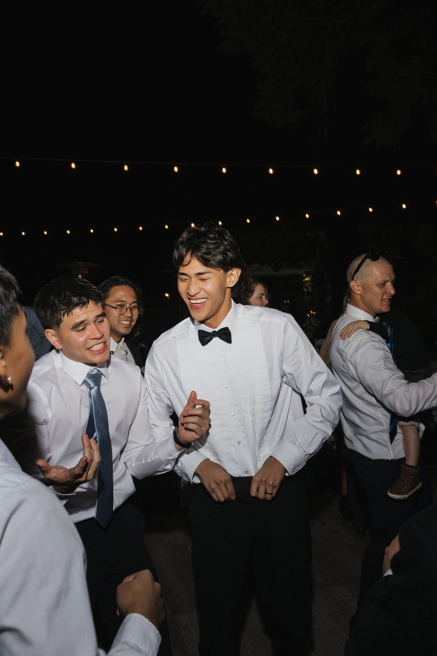 Groomsmen enjoying lively dance moments at nighttime wedding reception.