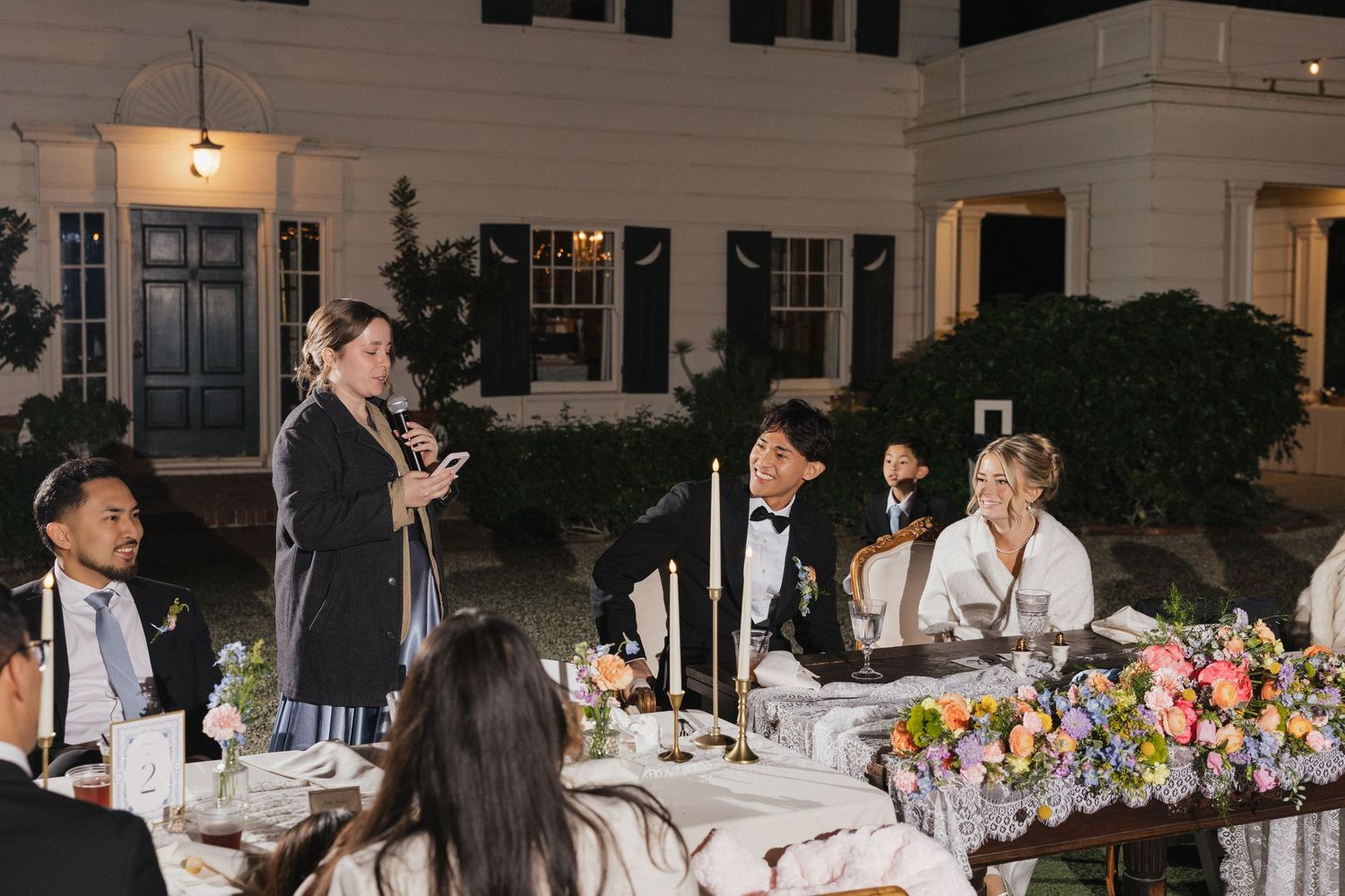 Wedding guests seated at elegant reception tables with colorful floral centerpieces during an evening celebration.