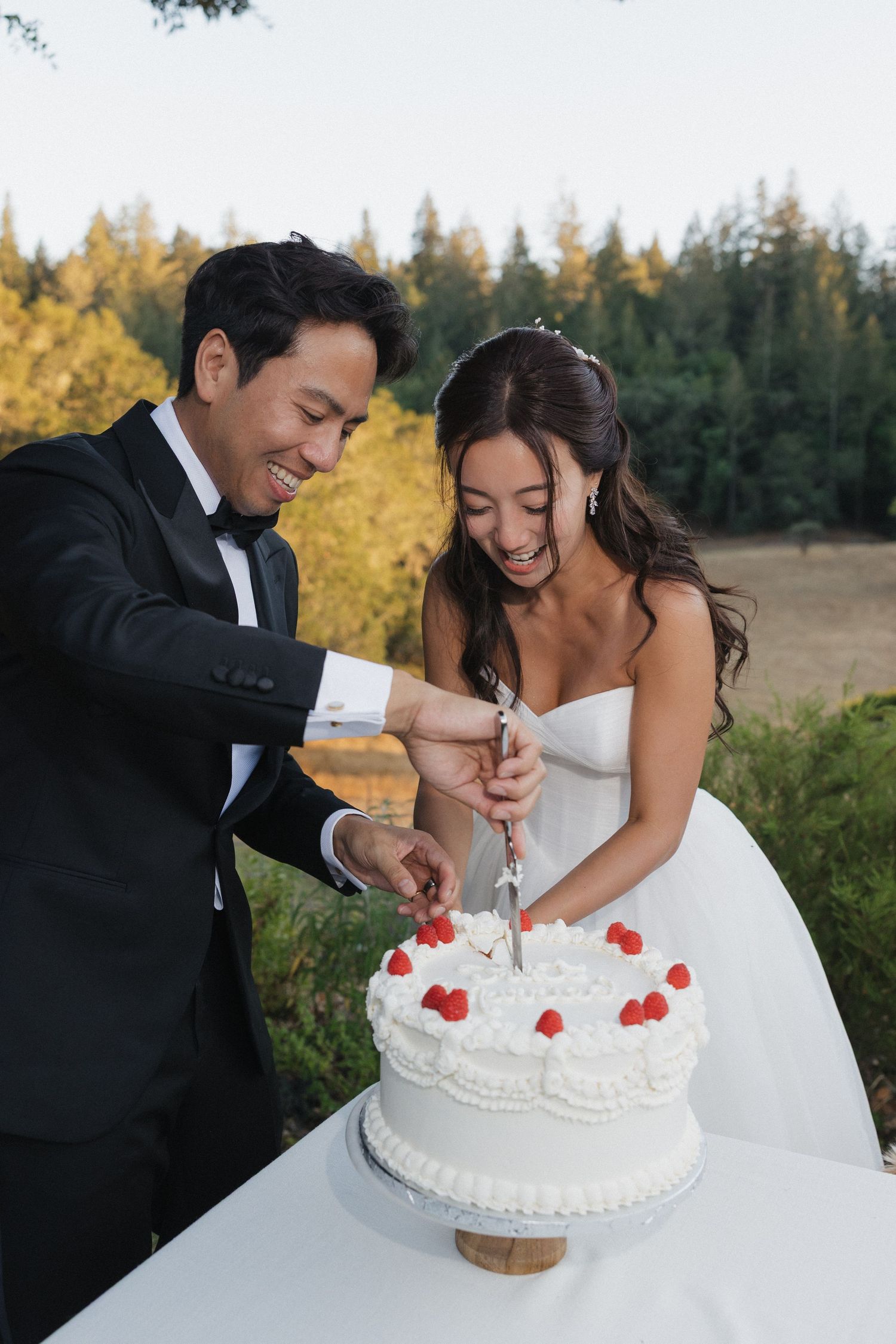 A couple cuts their white wedding cake decorated with red heart details.
