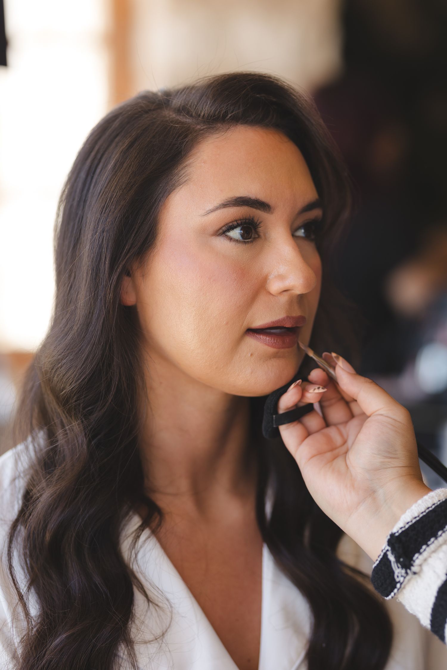 Professional makeup artist applies finishing touches during bridal preparations in a softly lit room.