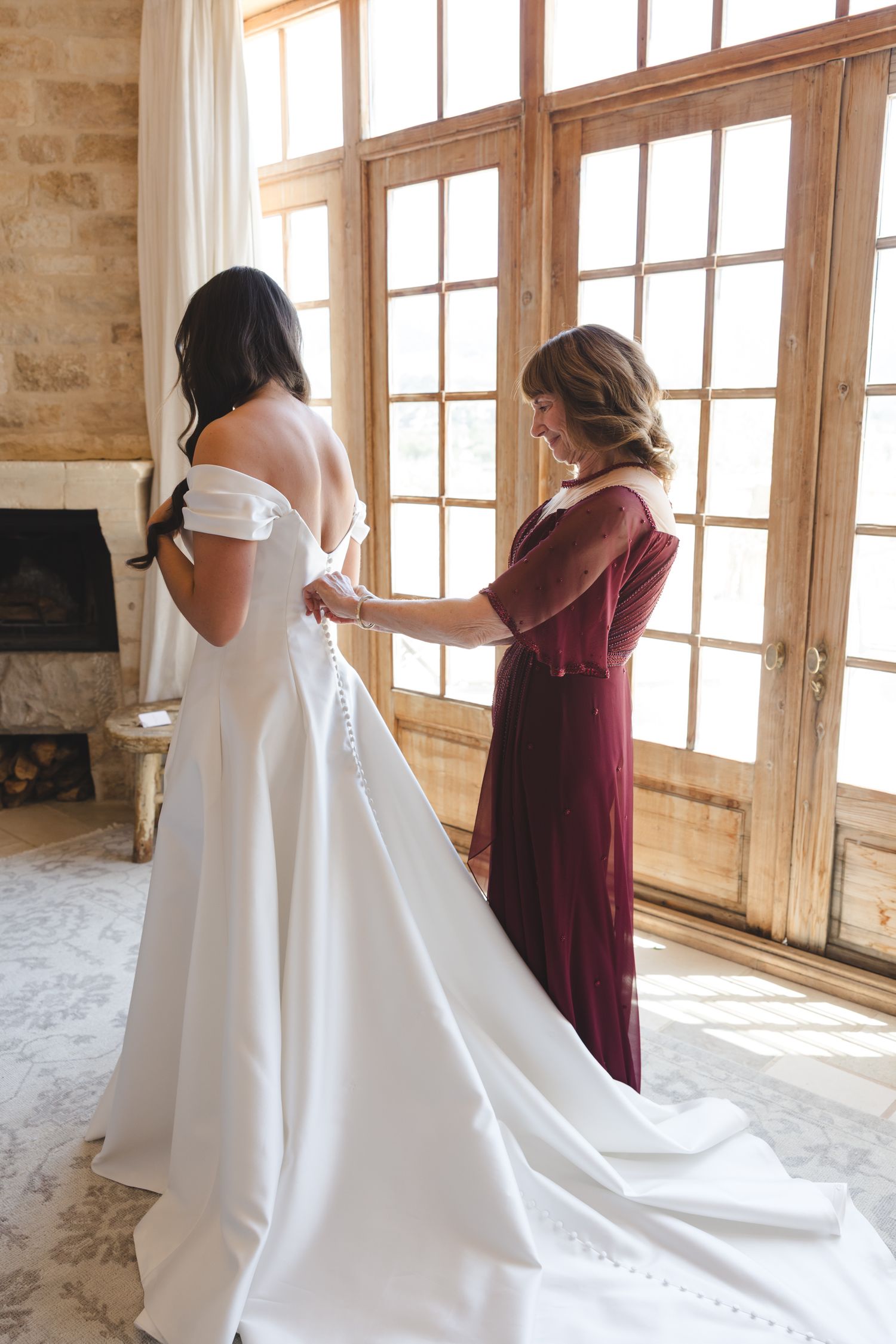 Final dress fitting in rustic room with large windows and stone walls.