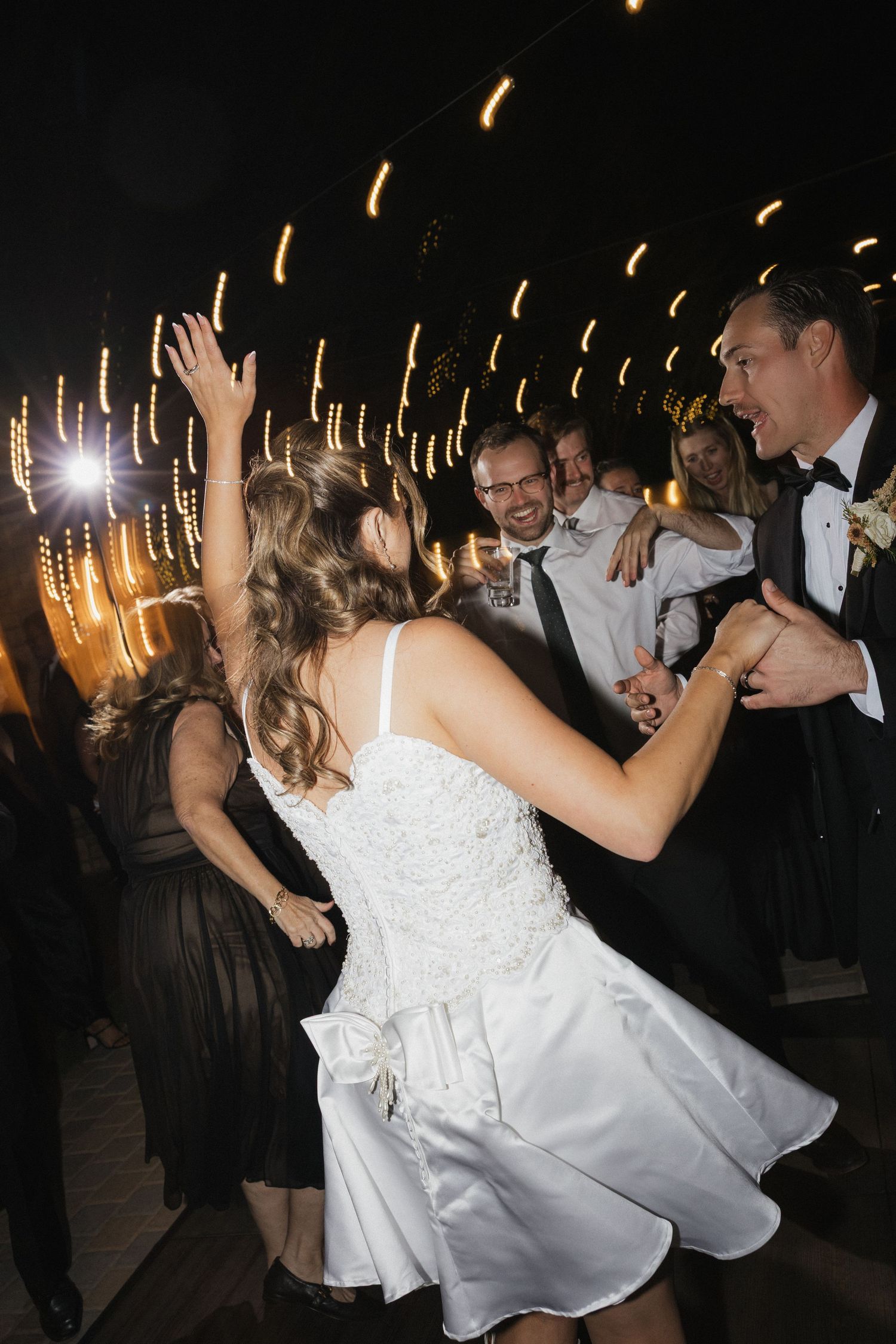 Wedding reception dance floor scene with bride in white dress twirling among party lights and guests.