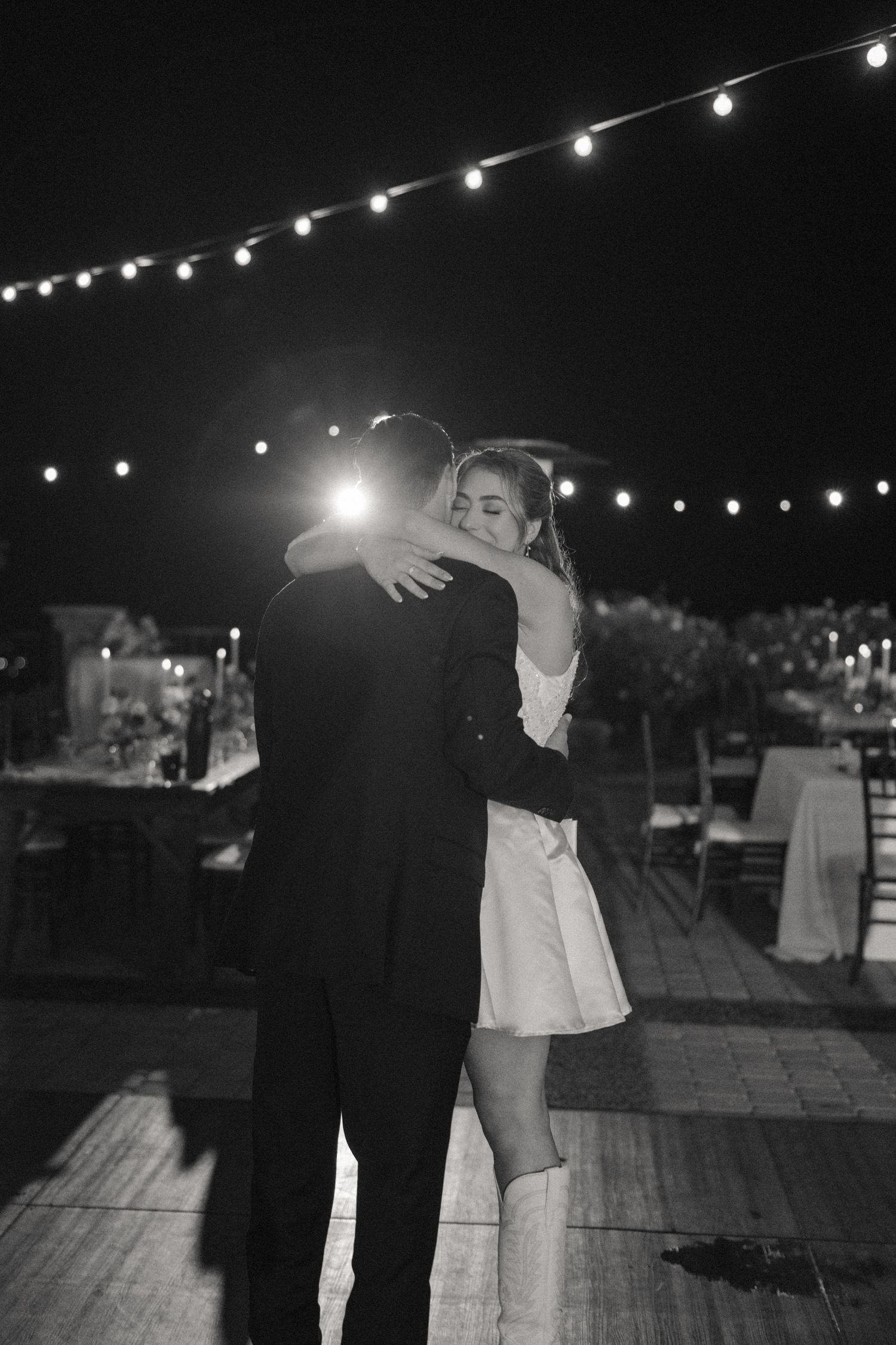 Romantic dance under string lights at outdoor evening wedding reception.