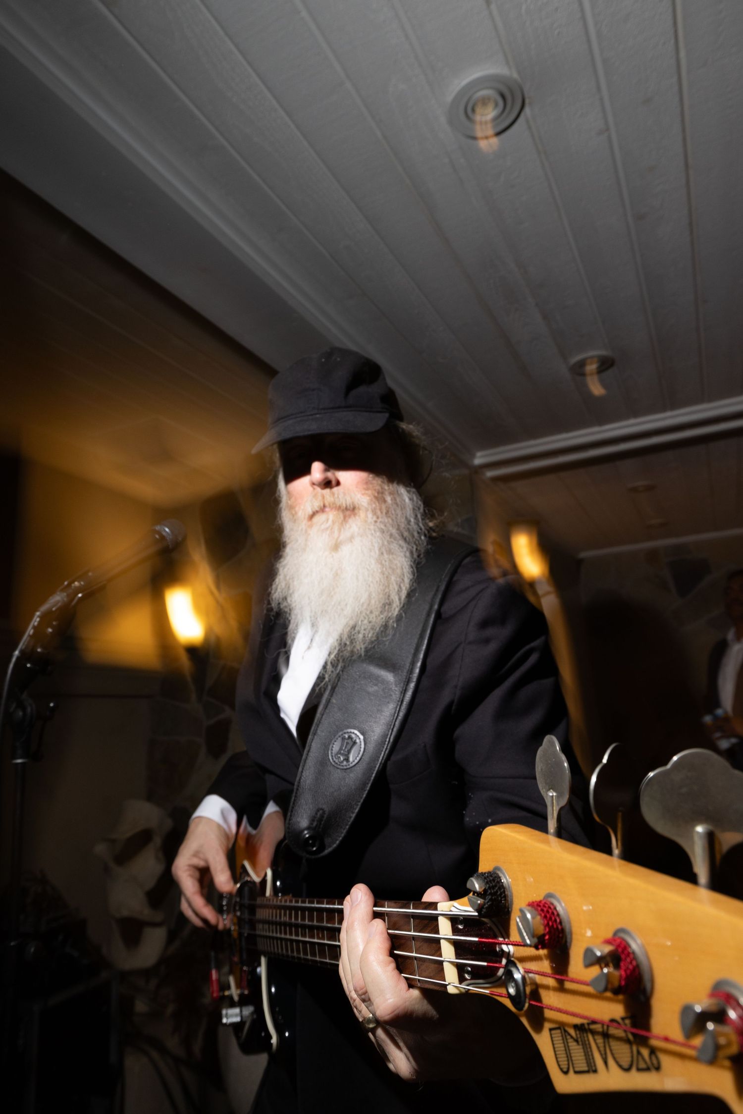 Bearded guitarist in black suit and cap performs live music at an intimate wedding reception.