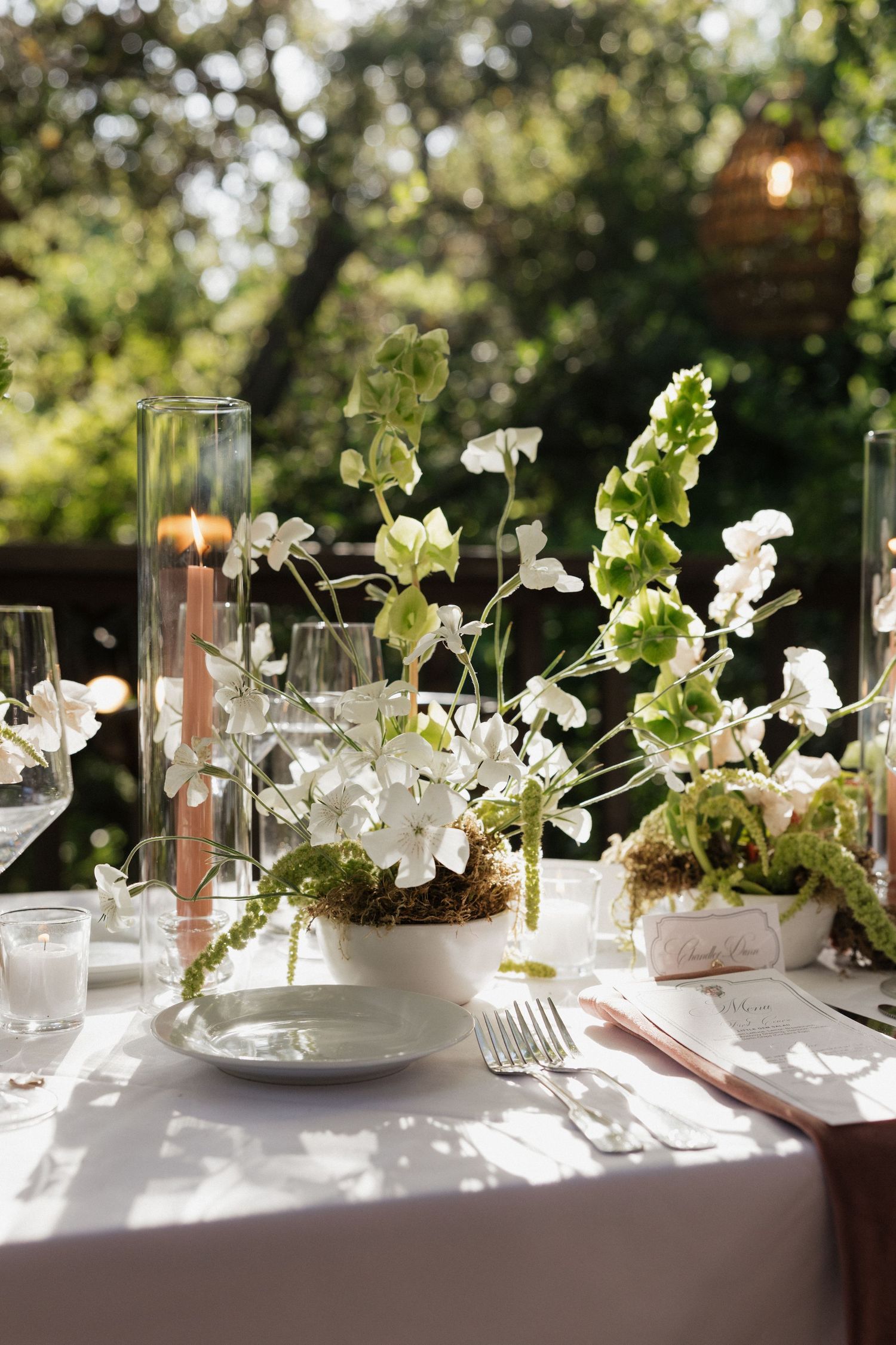 Elegant wedding tablescape with white floral centerpiece, taper candle, and lush greenery backdrop.