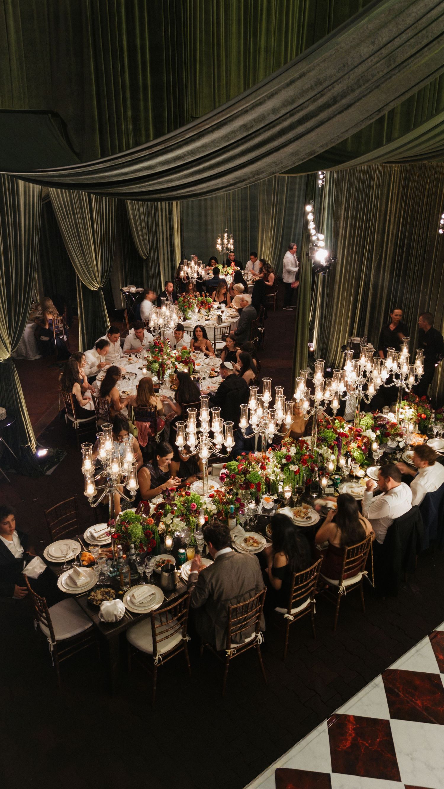 Elegant wedding reception setup with candlelit tables and dramatic dark draping in a formal dining space.