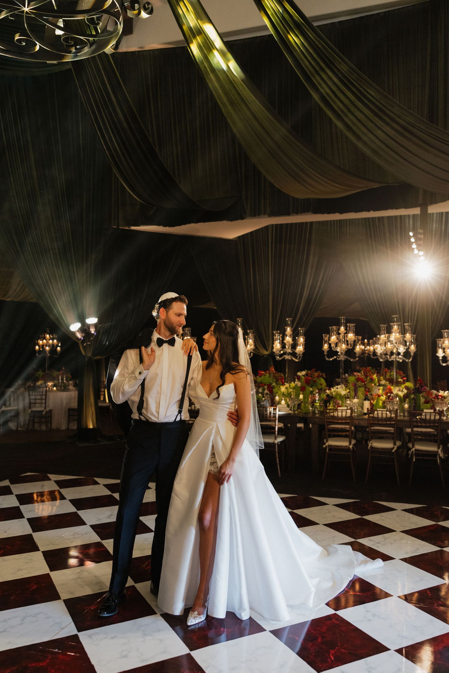 Couple dancing together on a black and white checkered dance floor under draped fabric ceiling at an elegant wedding reception.