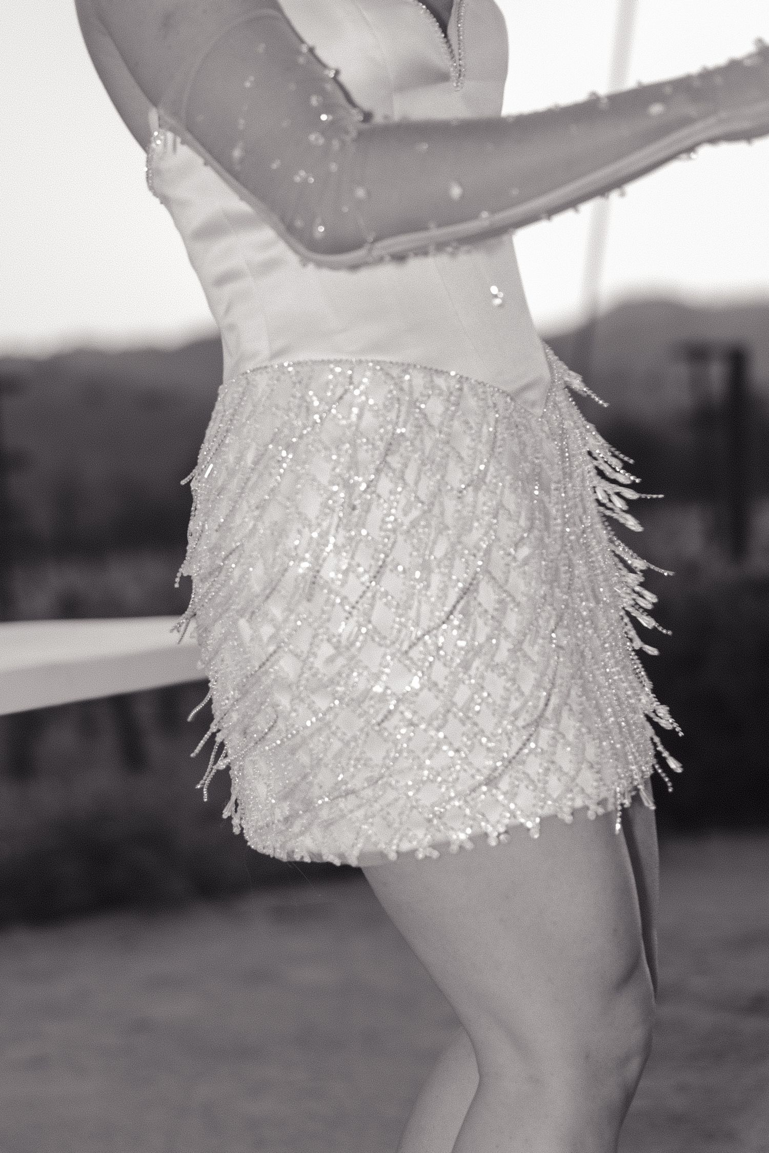 A person wearing a sparkly fringed flapper-style mini dress poses outdoors in a black and white photograph.