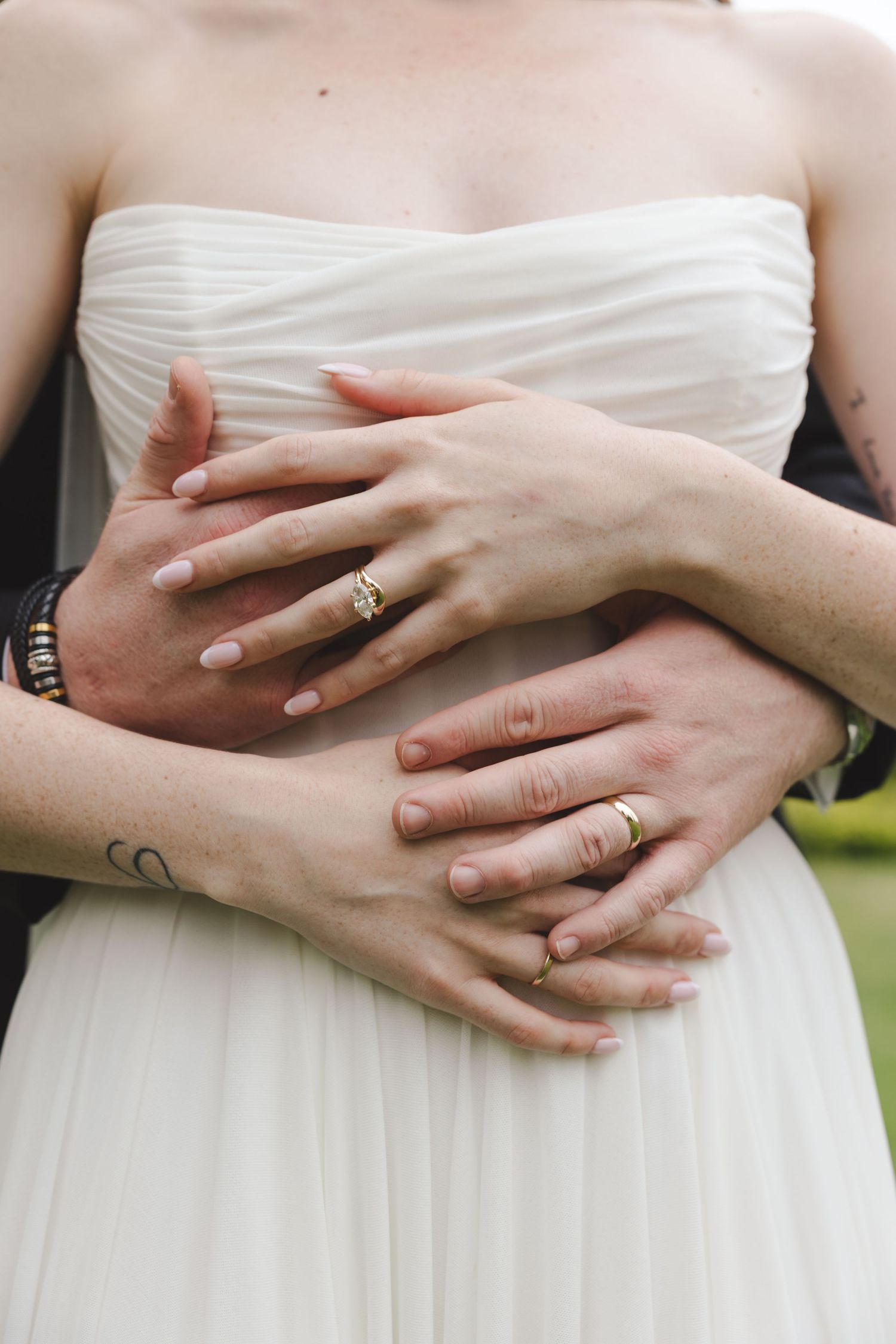 Hands wearing wedding rings embrace around a white wedding dress bodice, showcasing delicate details and romantic connection.
