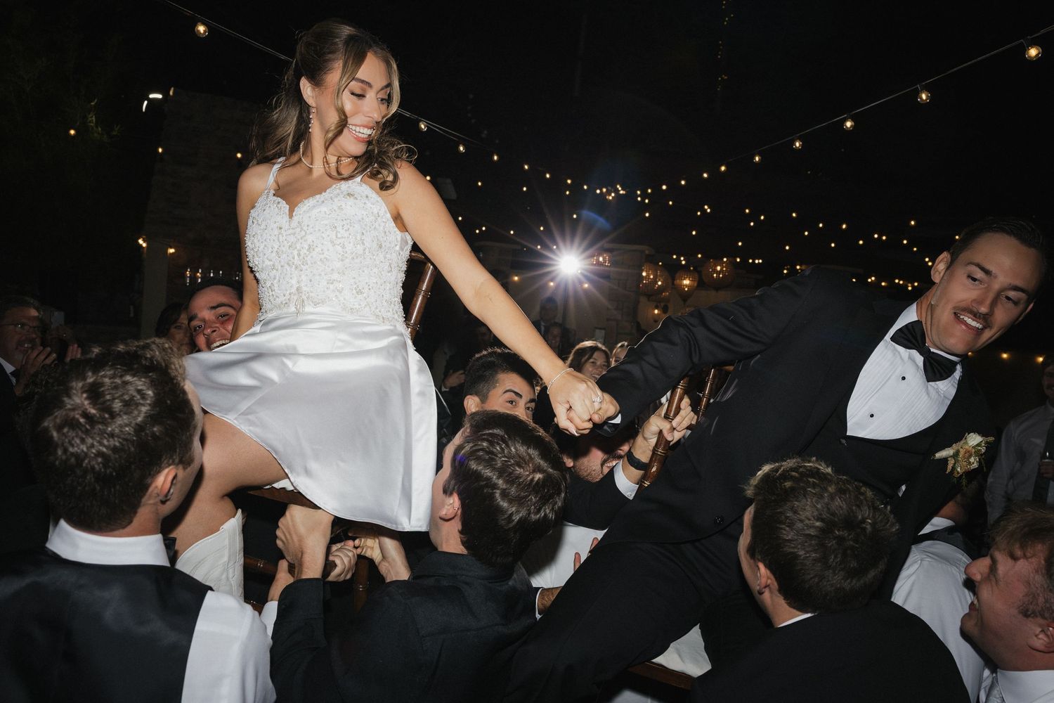 Lively dance floor scene at wedding reception with guests dancing under string lights.