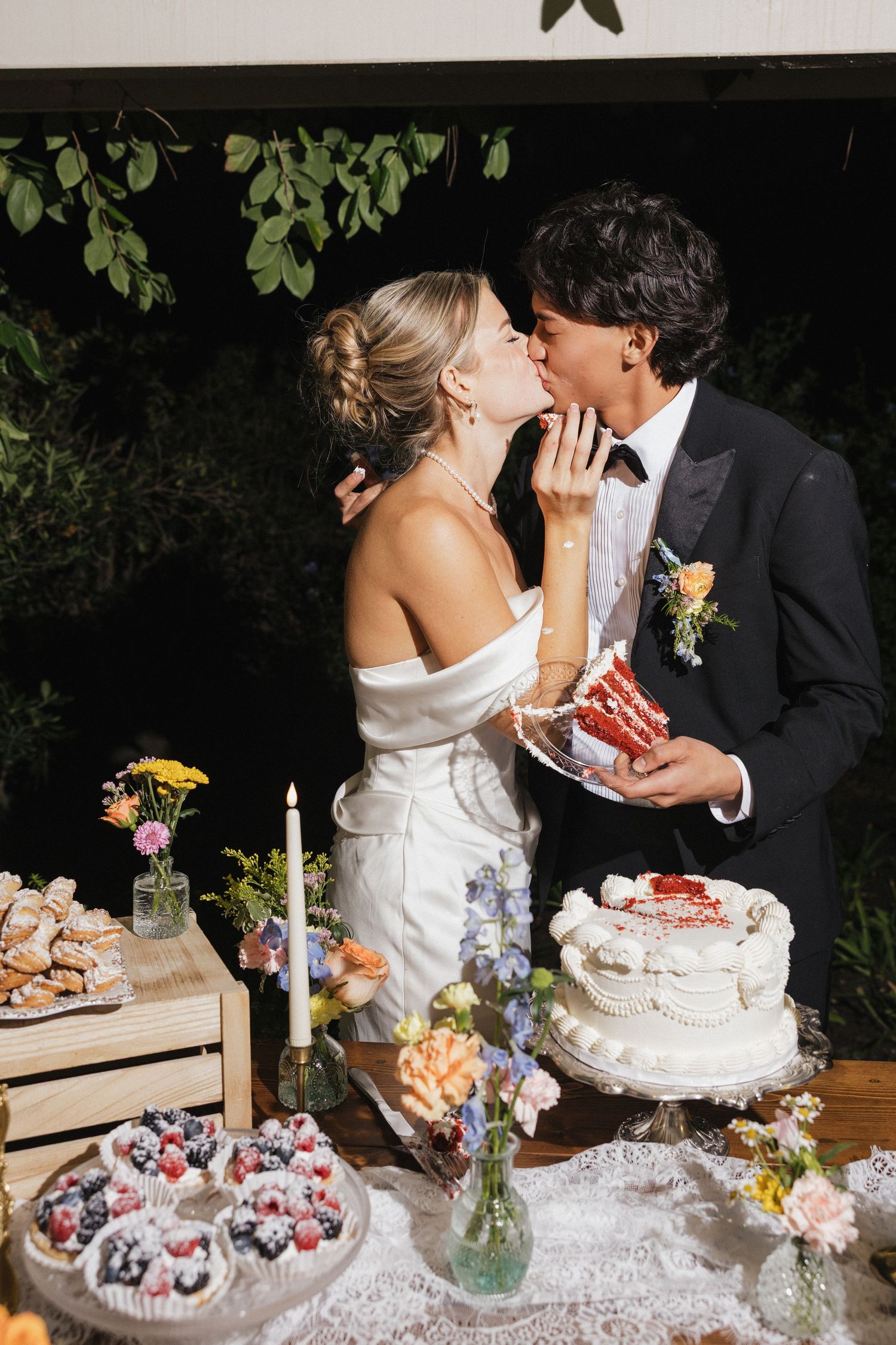 Wedding cake cutting scene with white tiered cake and colorful wildflower decorations on rustic table.