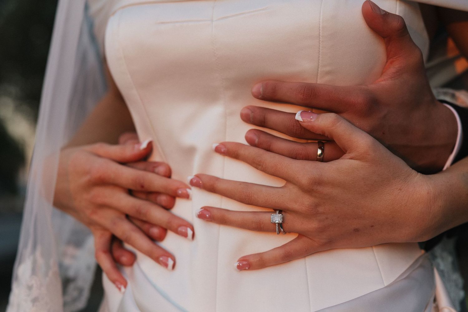 Close-up of hands displaying an engagement ring against a light background.