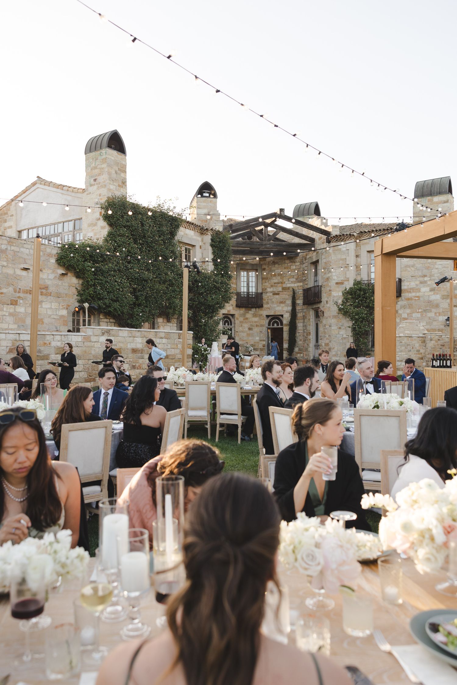 Elegant outdoor wedding reception at a rustic stone venue with tables decorated with white floral centerpieces.