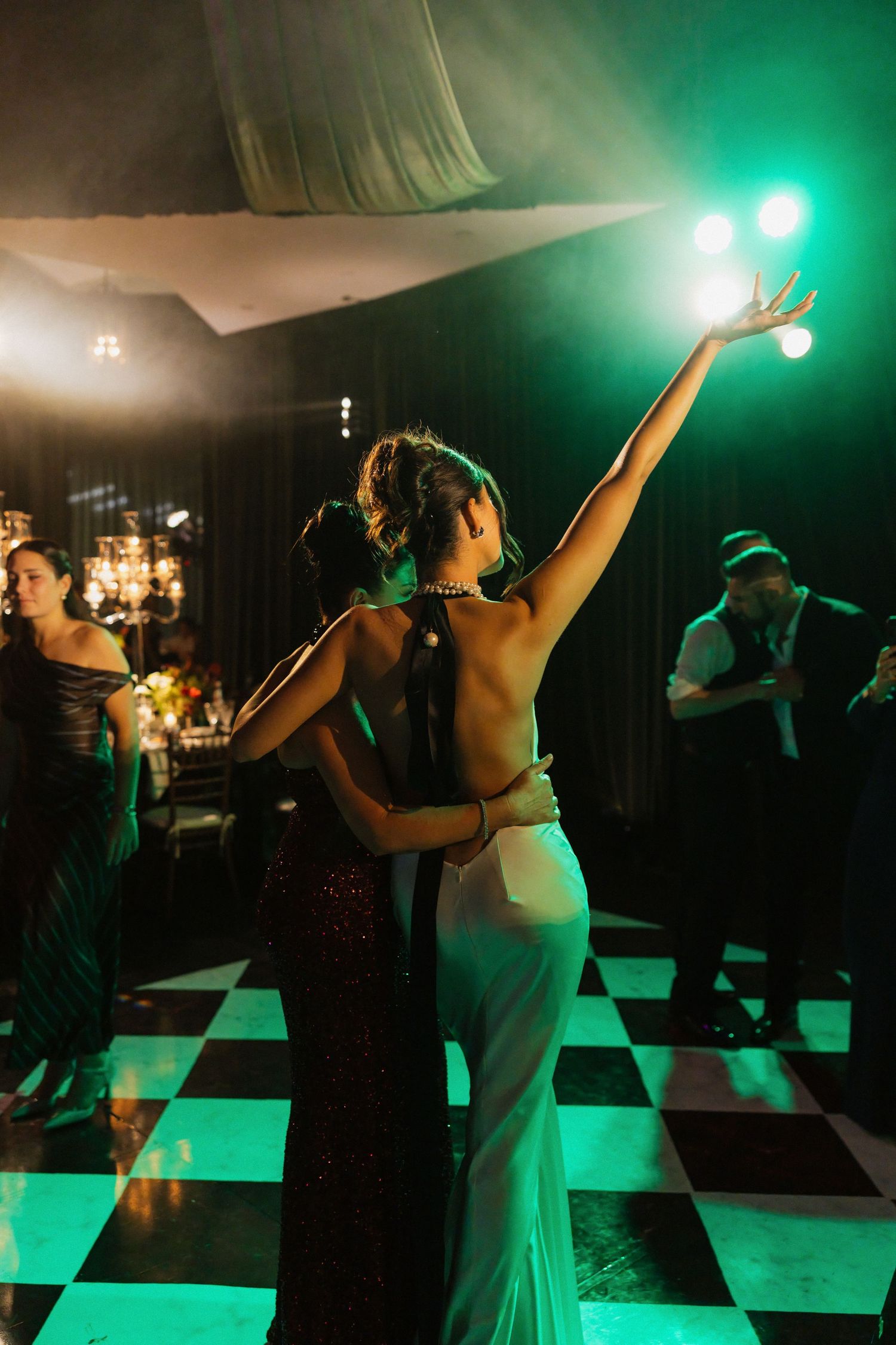 Wedding party dancing on a dark dance floor illuminated by dramatic green stage lighting.