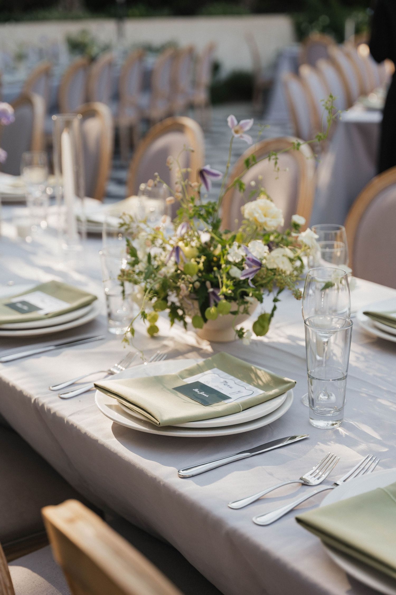Elegant table settings with white plates, silver cutlery, and delicate floral centerpieces on a pale gray tablecloth.