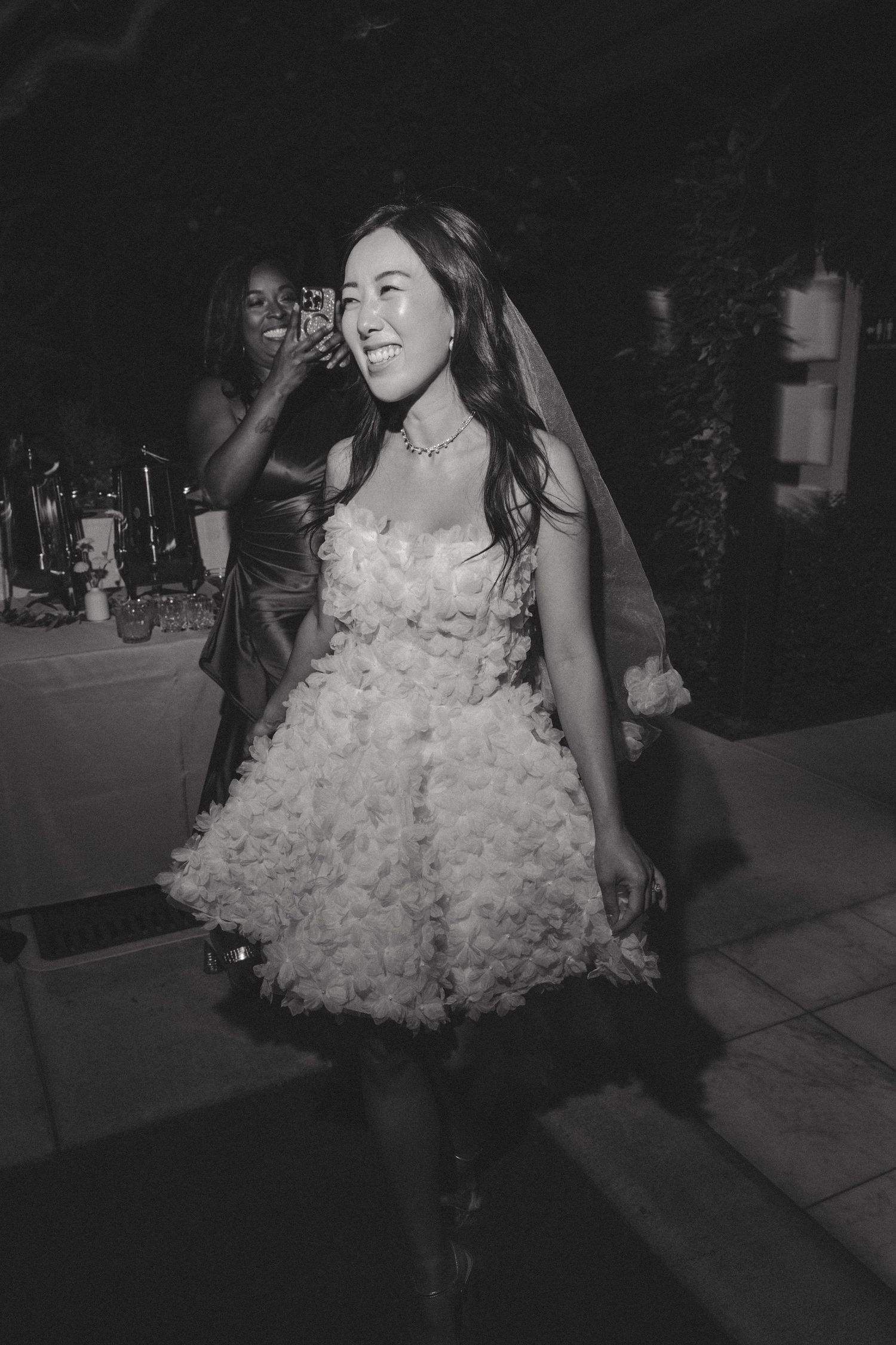 Black and white photo of someone in a ruffled white dress dancing at a wedding reception.