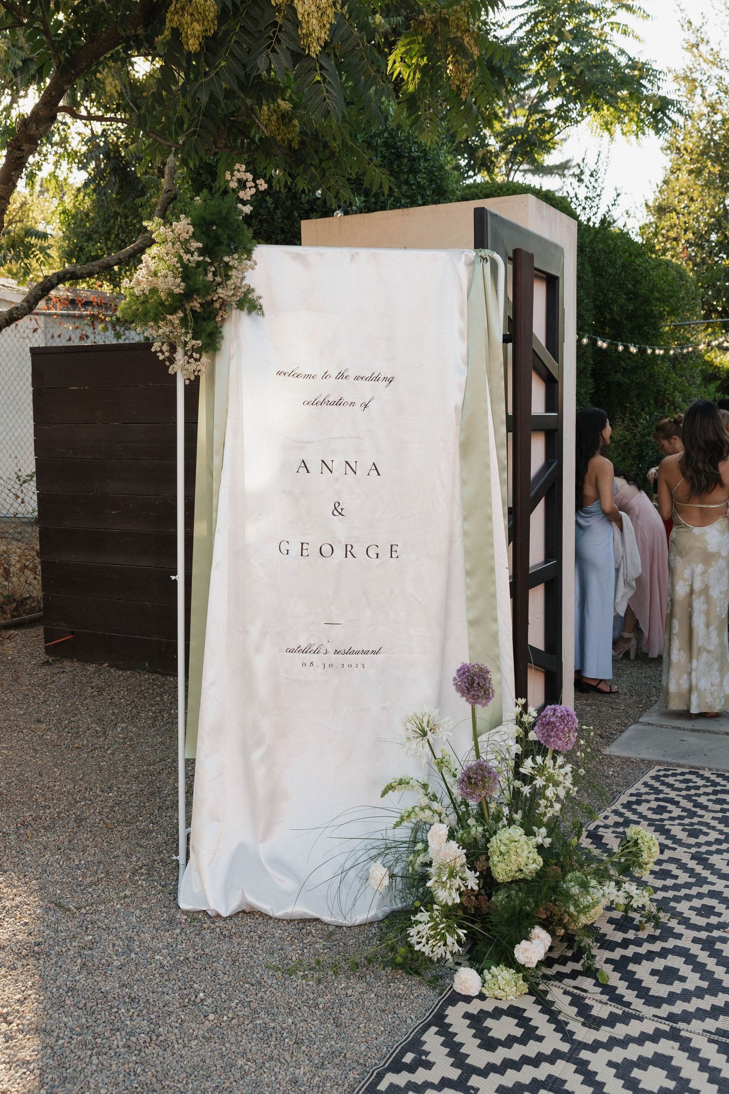 Wedding welcome sign display with white fabric backdrop and floral arrangements.