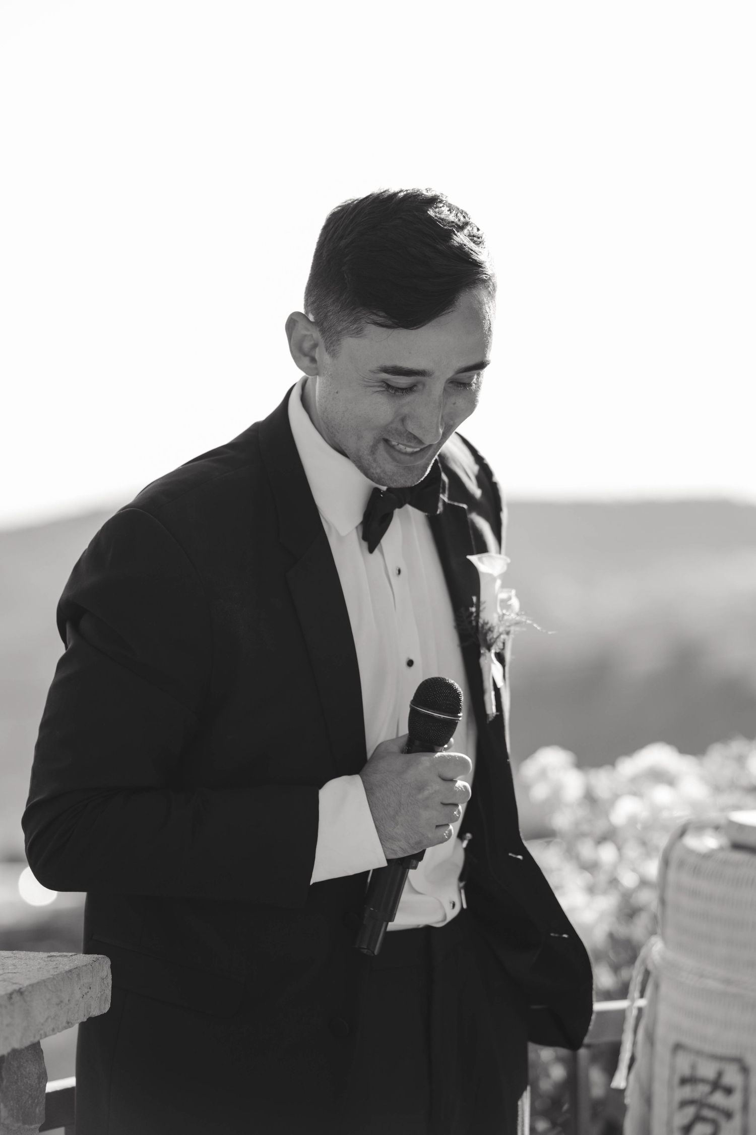 Emotional wedding speech moment captured in black and white as speaker smiles into microphone.