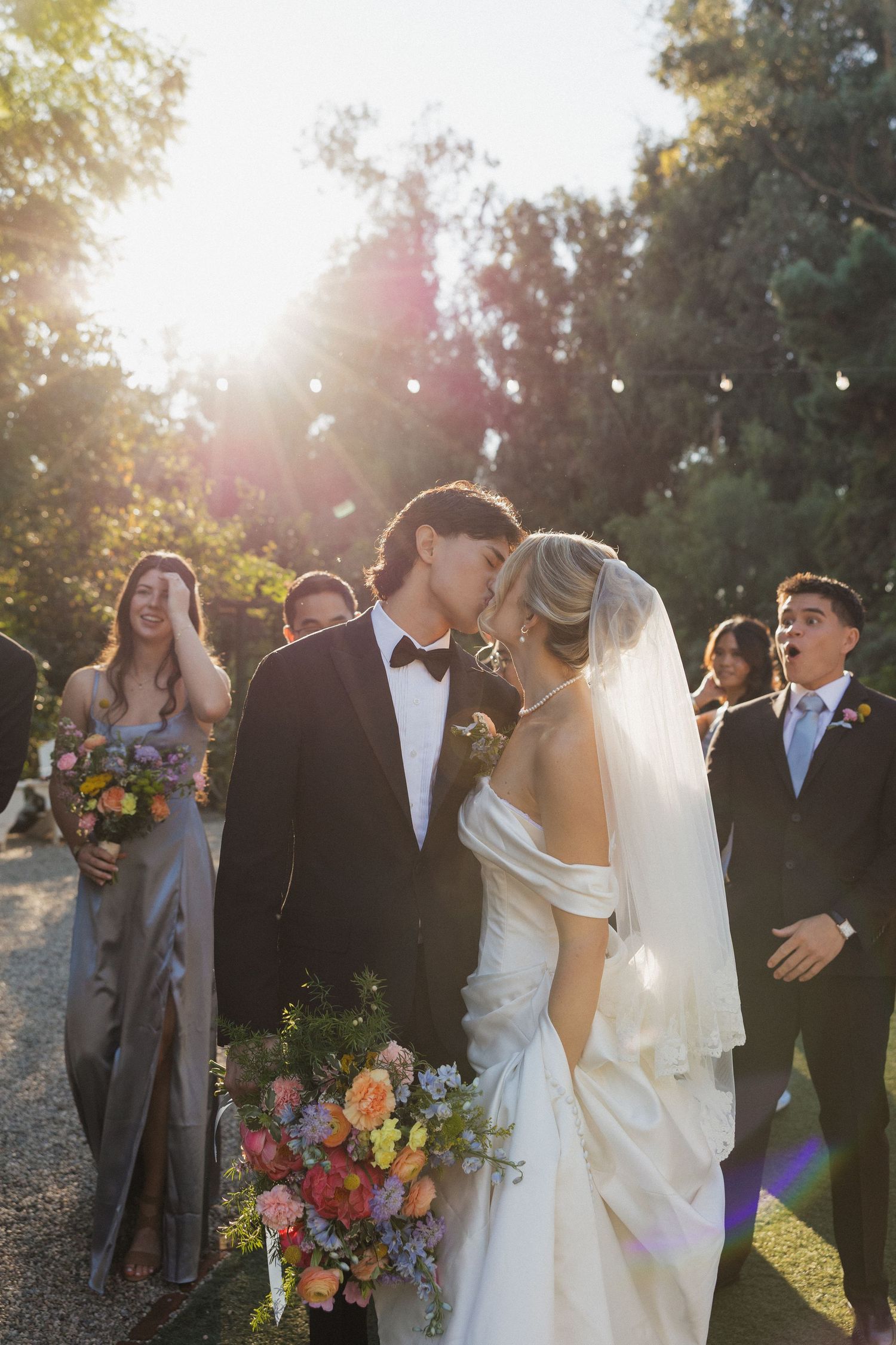 A wedding party celebrates outdoors at sunset with vibrant flowers and joyful expressions.