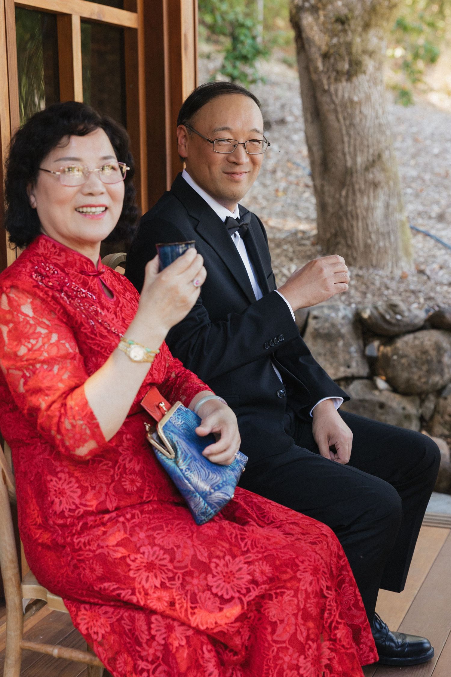 Group wearing formal attire including red traditional dress seated in a wooden gazebo.