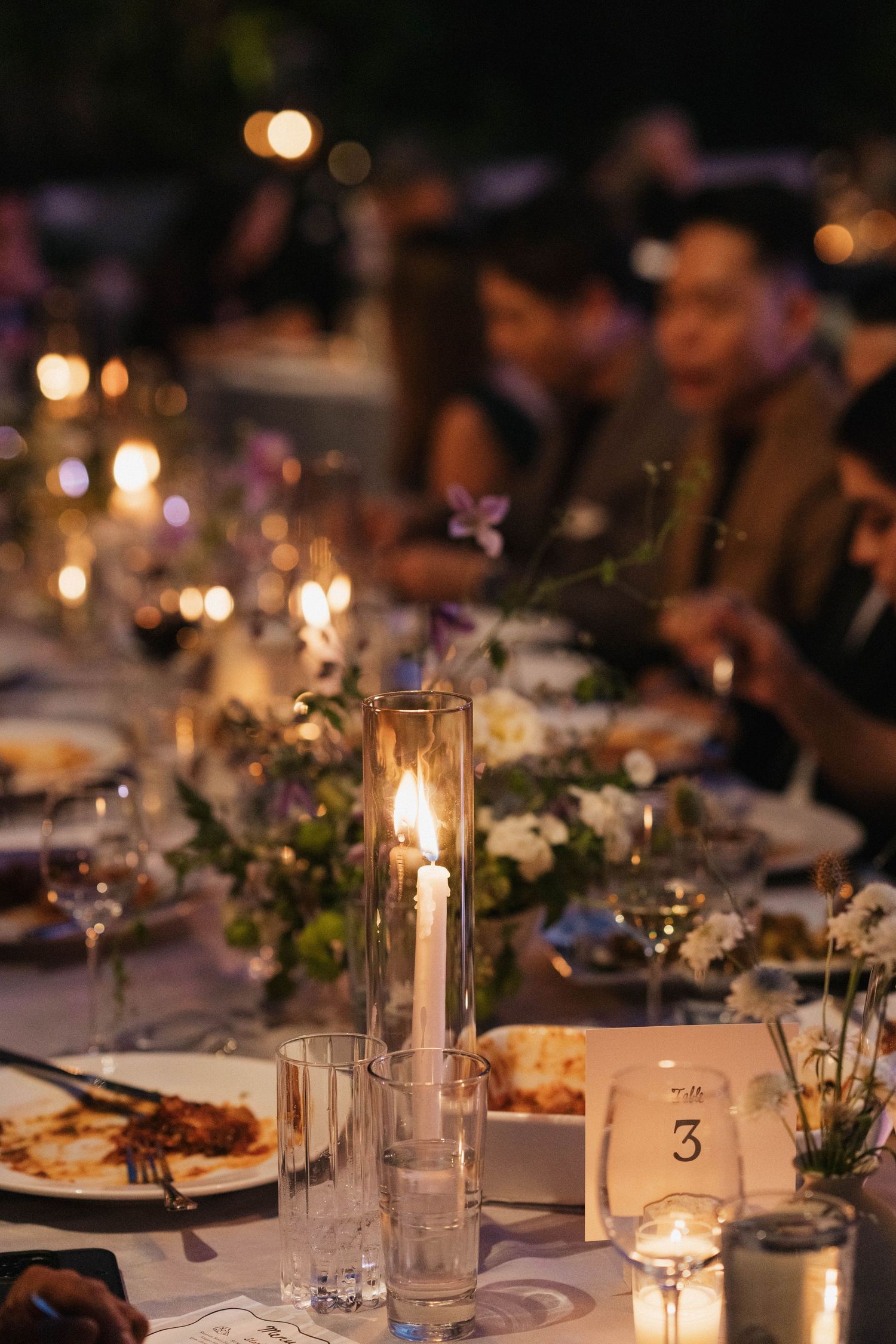 Romantic candlelit wedding reception tables decorated with greenery and glowing centerpieces.