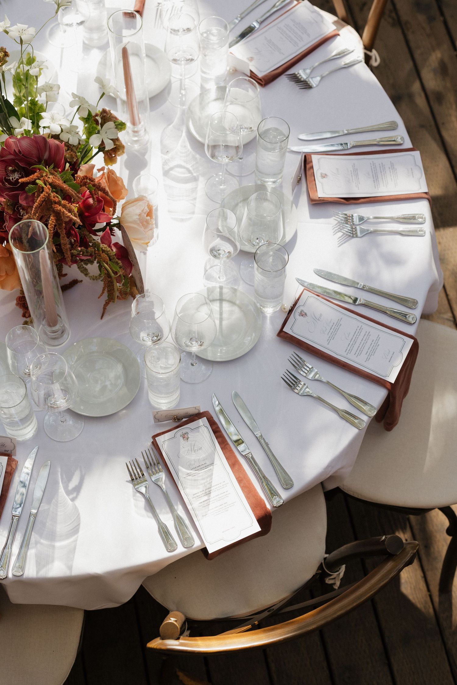 Aerial view of round wedding reception table with white linen, menus, glassware, and floral centerpiece.