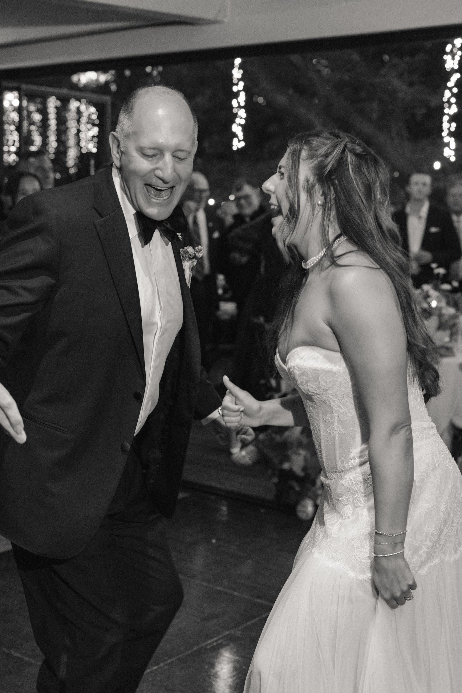 Black and white photo of a laughing bride in strapless gown dancing joyfully with a man in a tuxedo.