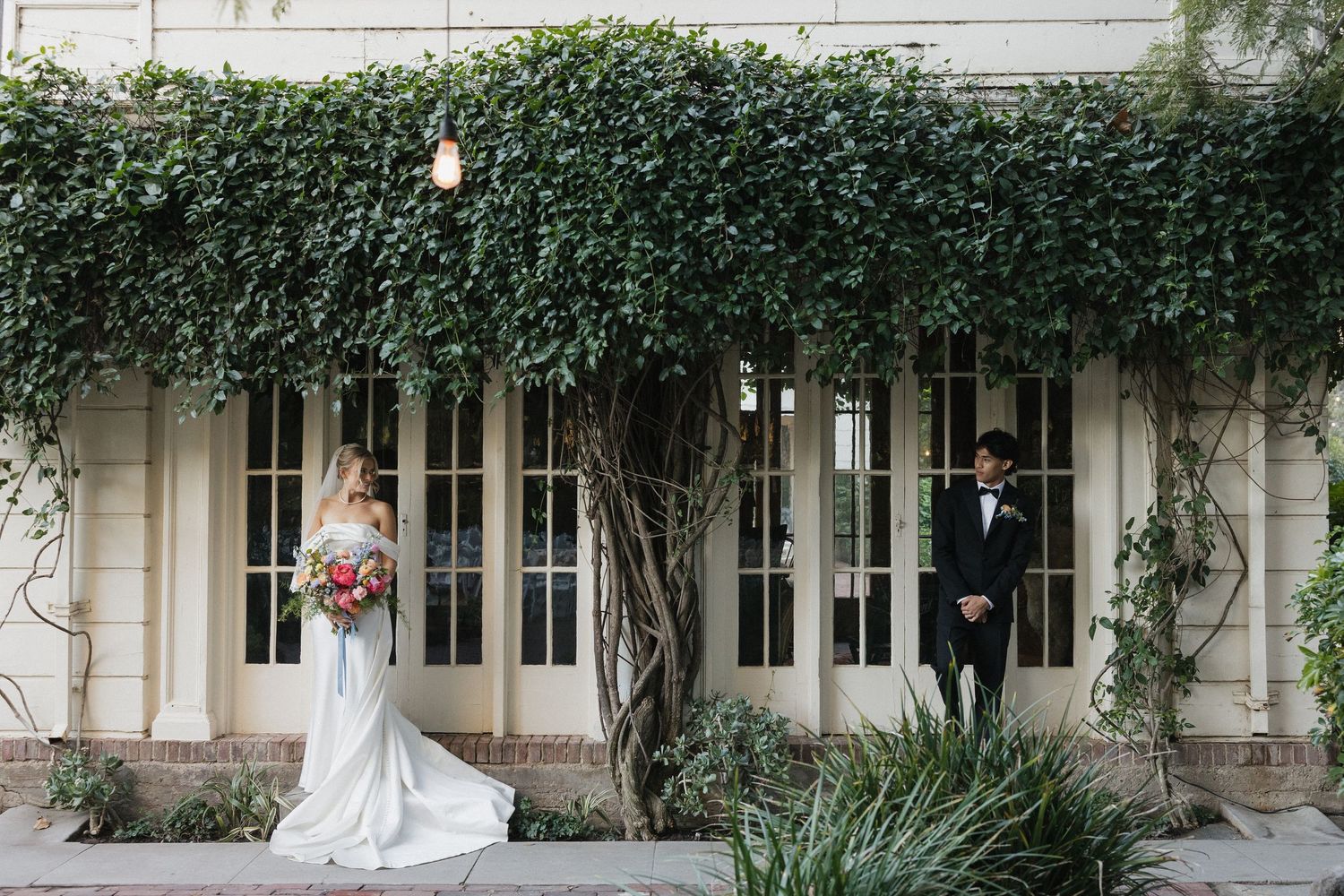 String lights illuminate an elegant outdoor wedding venue with white pillars and lush greenery creating a romantic ambiance.