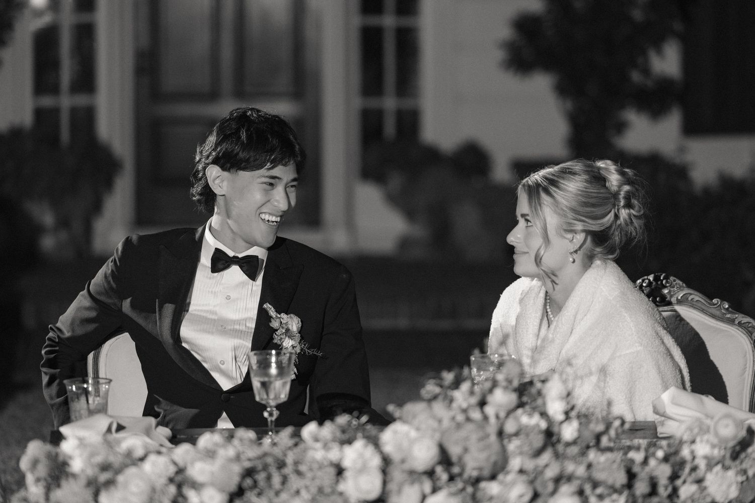 Black and white photo of an elegant wedding reception with floral centerpieces and formal place settings.