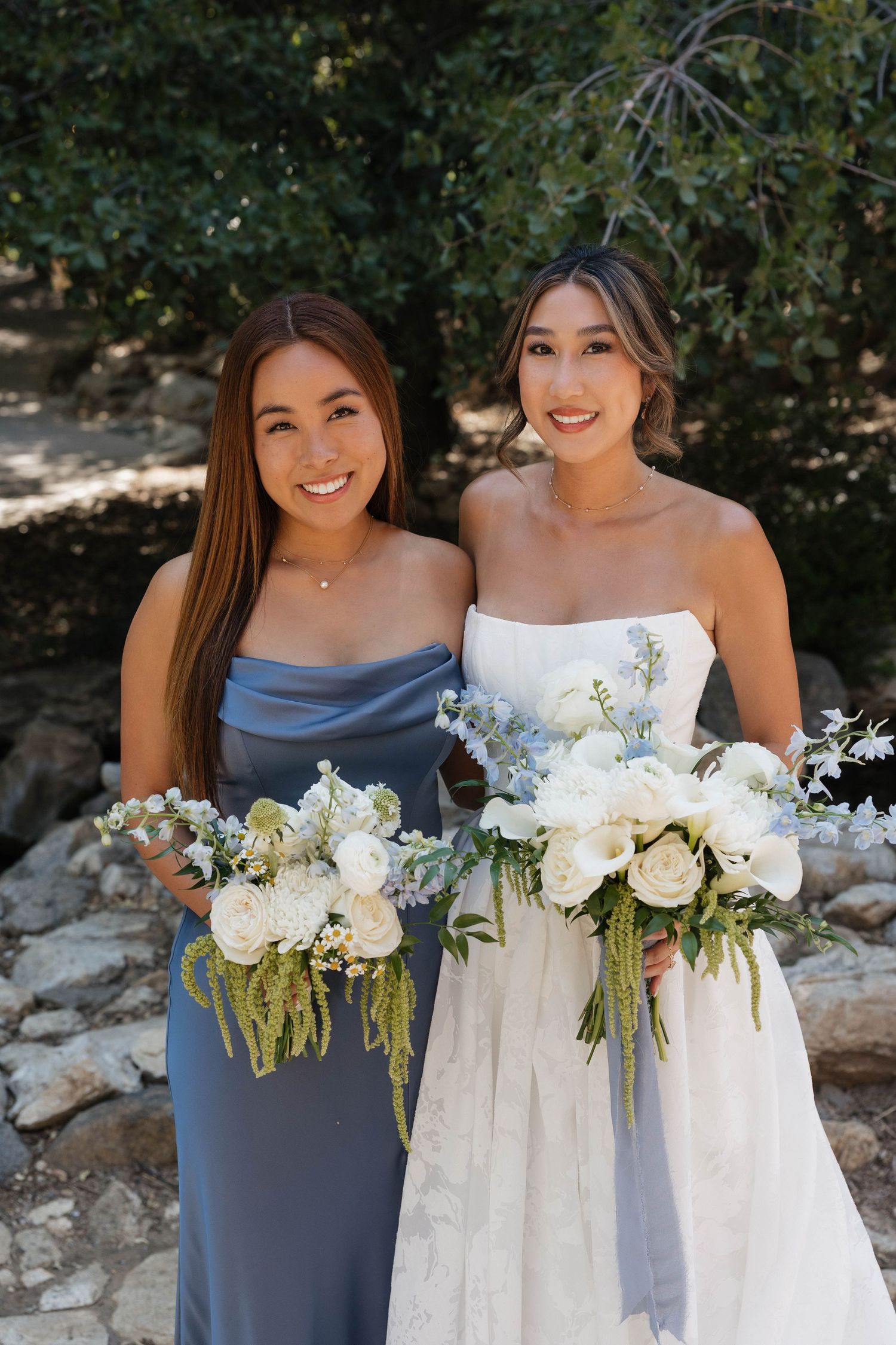 Bridesmaids in dusty blue dresses hold elegant white floral bouquets at outdoor wedding.