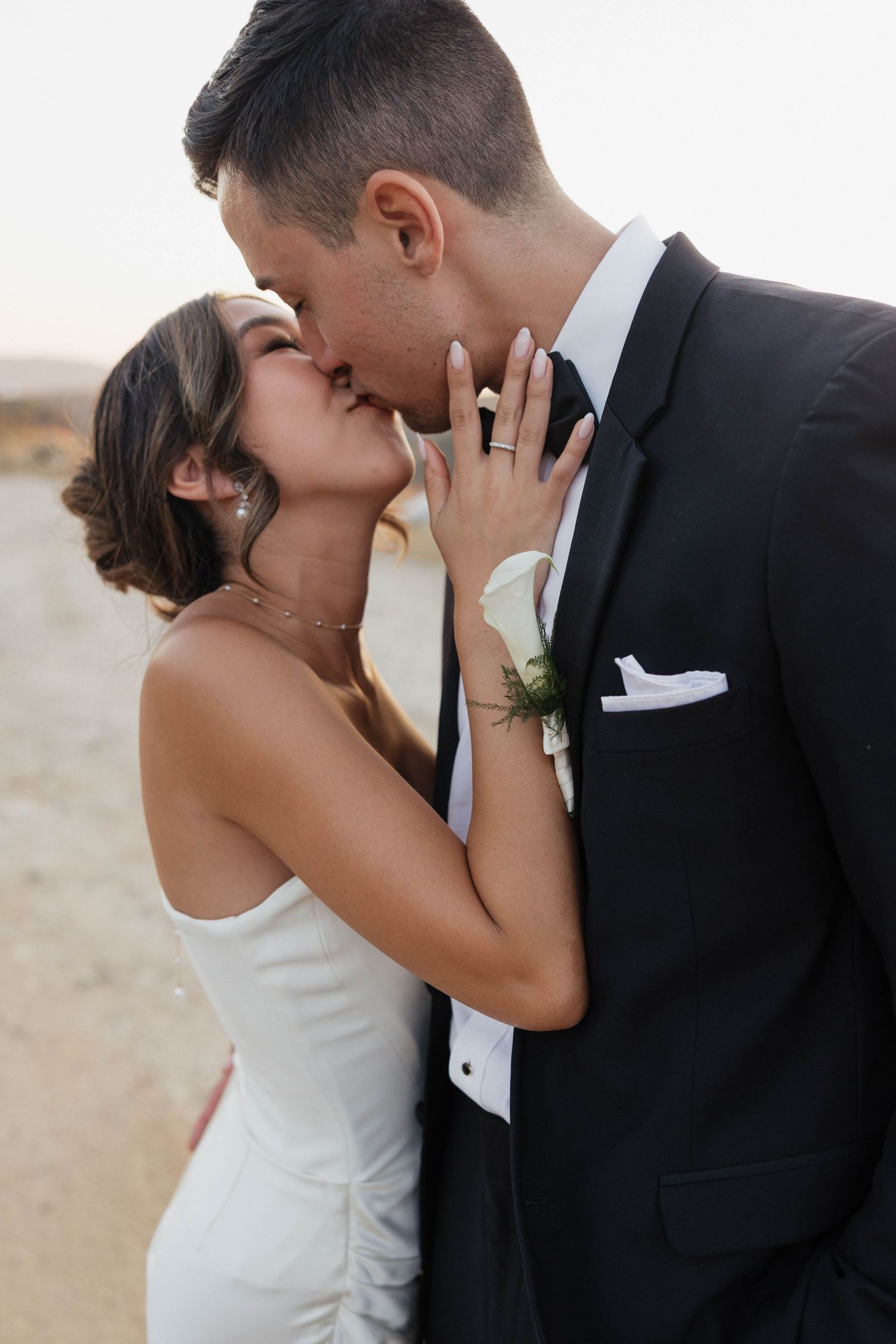 Romantic wedding couple sharing intimate kiss against natural outdoor background.
